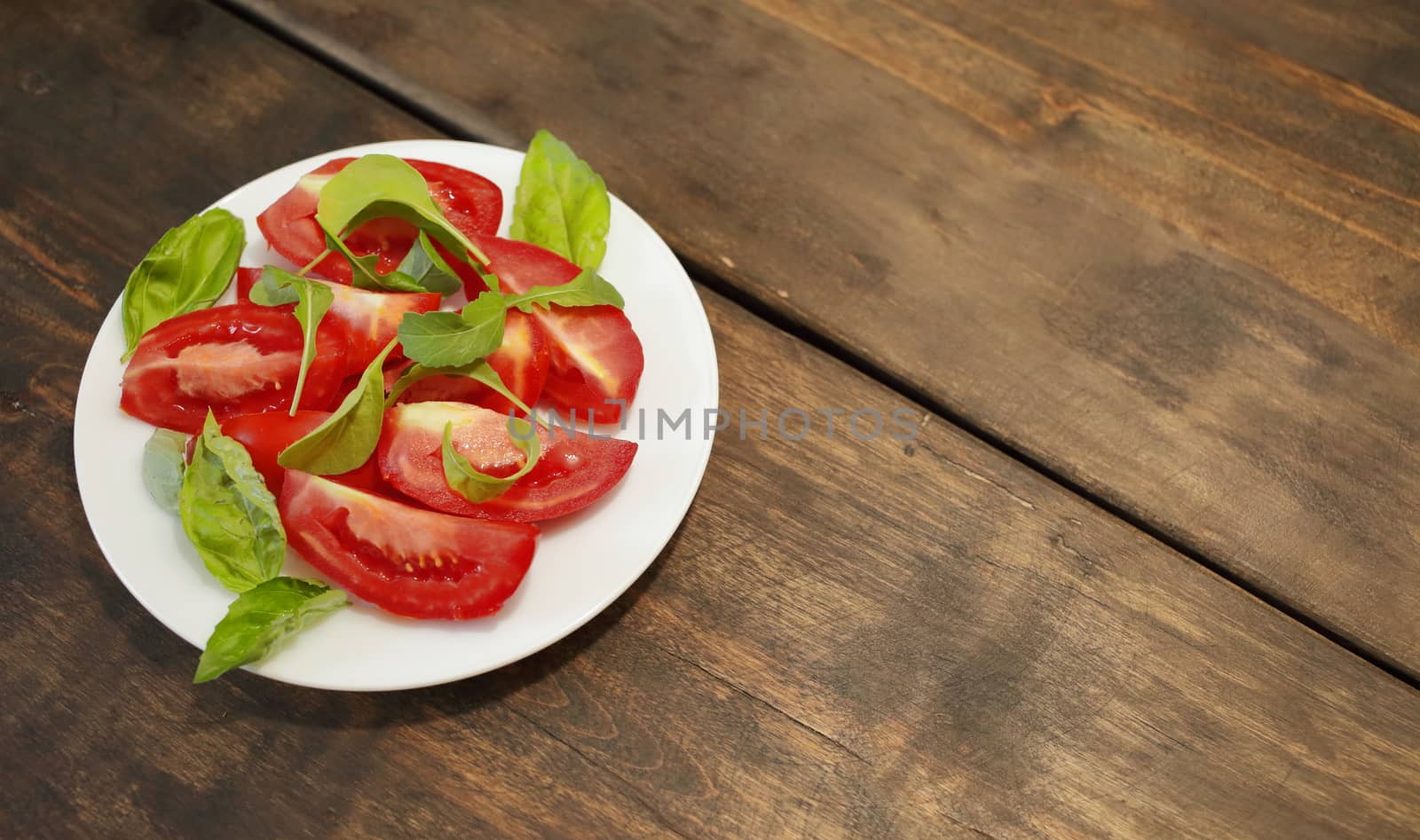 Sliced tomatoes with lettuce on a white plate. Healthy eating concept by selinsmo