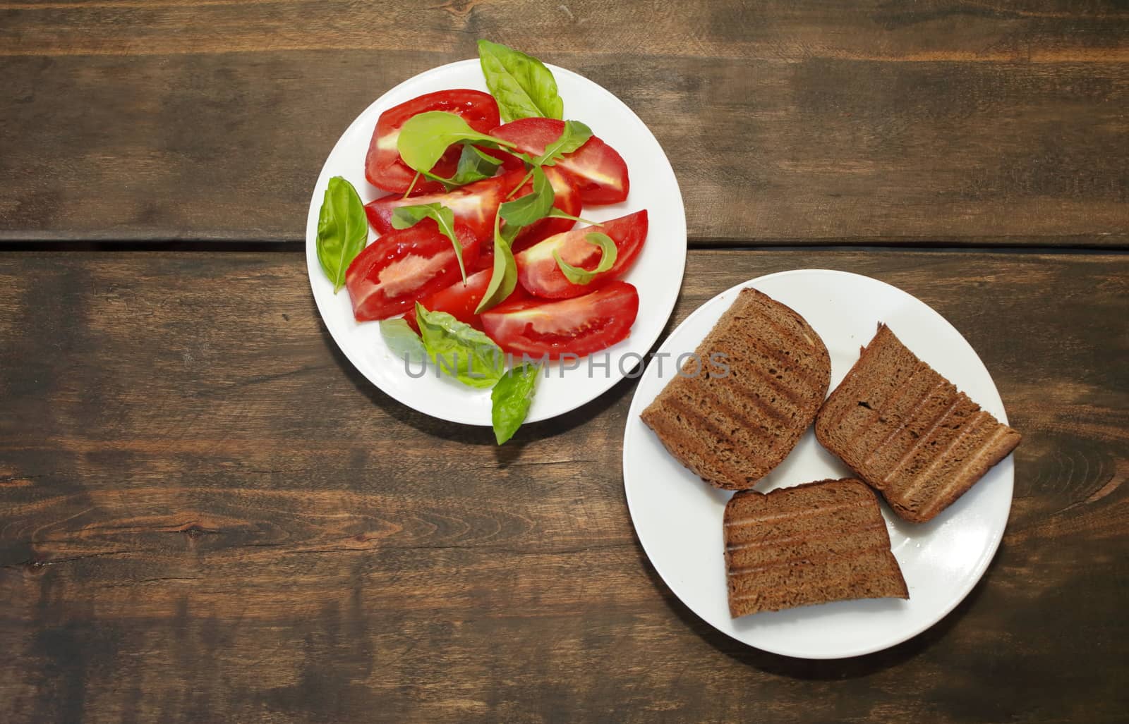 Sliced tomatoes with lettuce on a white plate. Fresh bread toast. Healthy eating concept by selinsmo