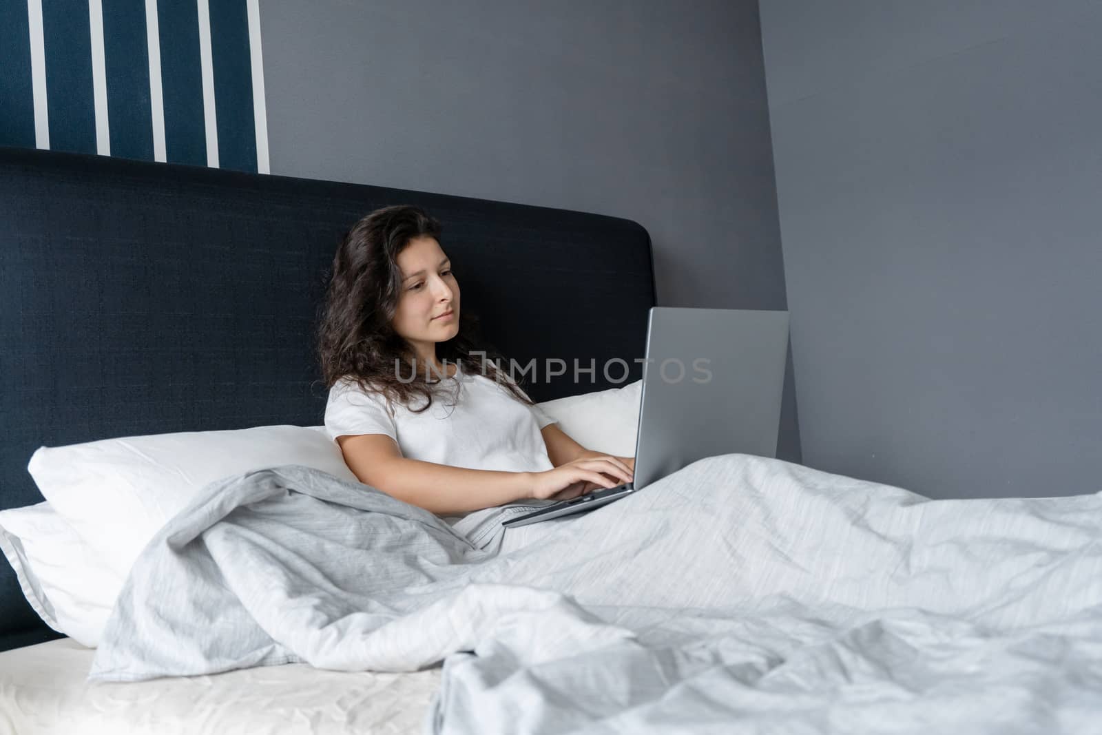 Beautiful brunette girl in bed with a laptop. Work from morning to late night. Electronic gadgets before bedtime or in the morning