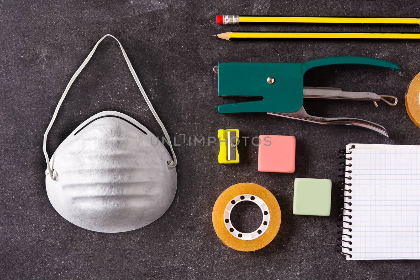 Assorted of school supplies and protective face mask on black slate. Back to school concept.