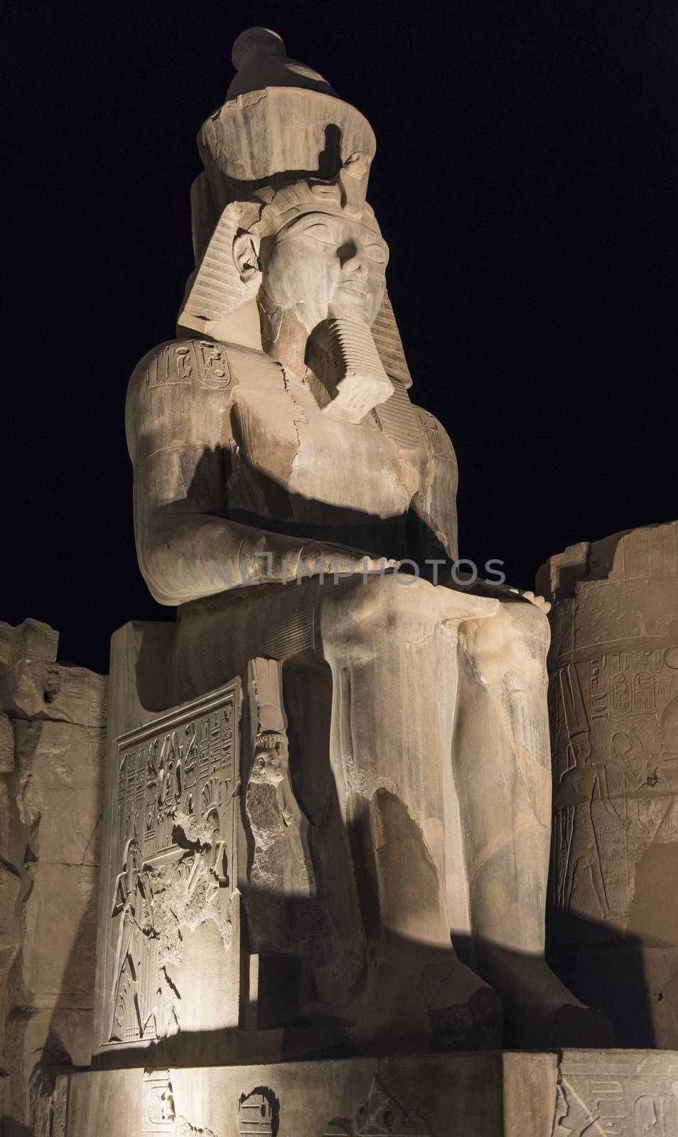 Ancient sitting statue of Ramses II in Luxor Temple lit up at night