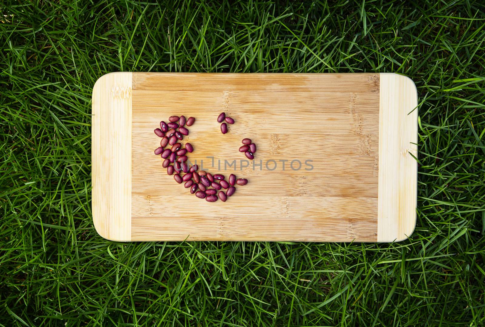 smiley face made of red kidney on top of a wood cutting board, laying on top of green grass