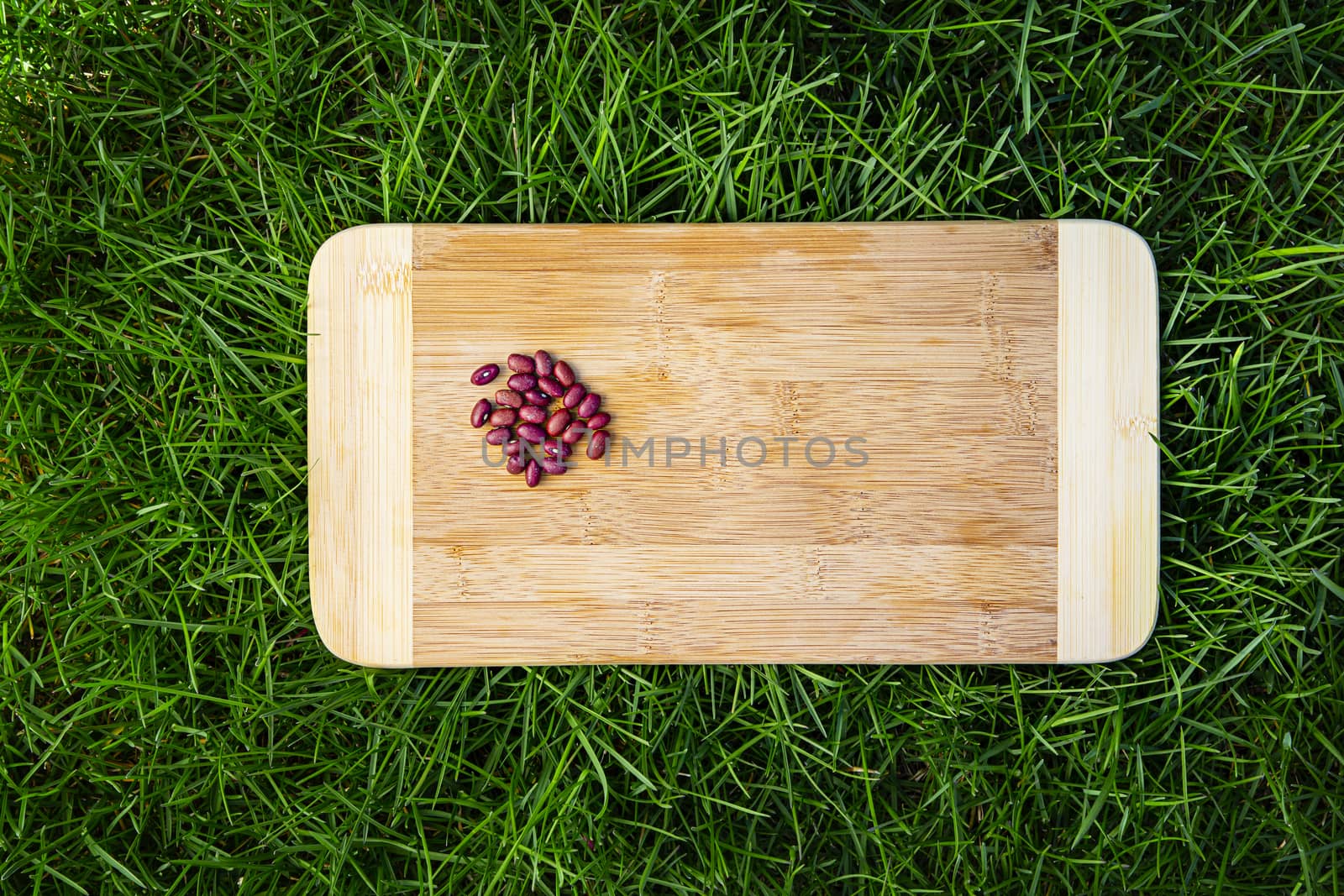small heap of red kidney bean on top of wood cutting board, sitting on green grass