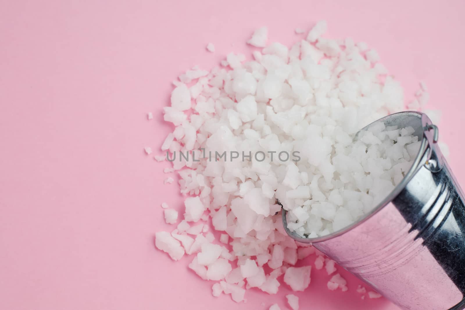 Sea salt in a tin bucket on pink background for seasoning or preserving food