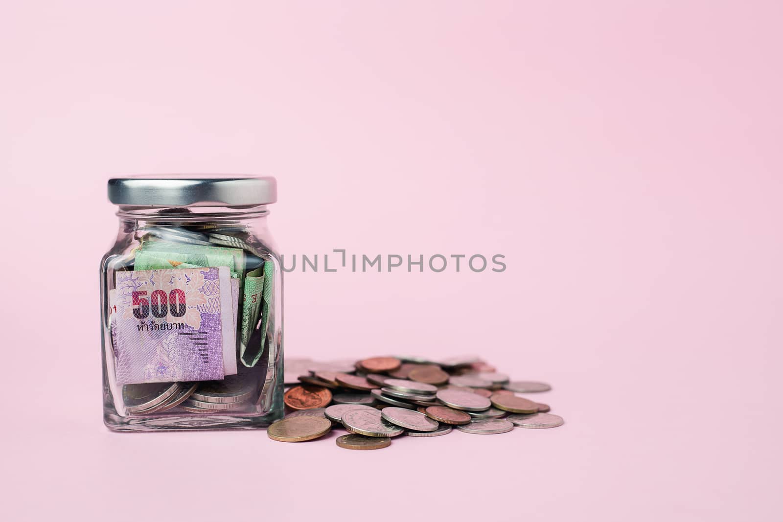 Thai currency banknote and coins in the glass jar on pink background for business, finance, investment and saving money concept