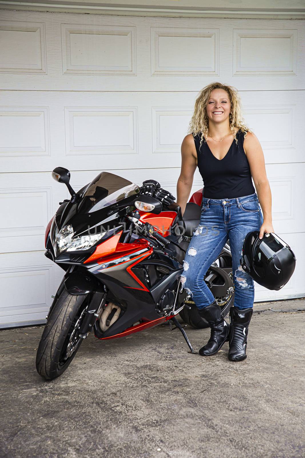 Young woman in her twenties, standing in from of a sport motocycle, in front of a garage door