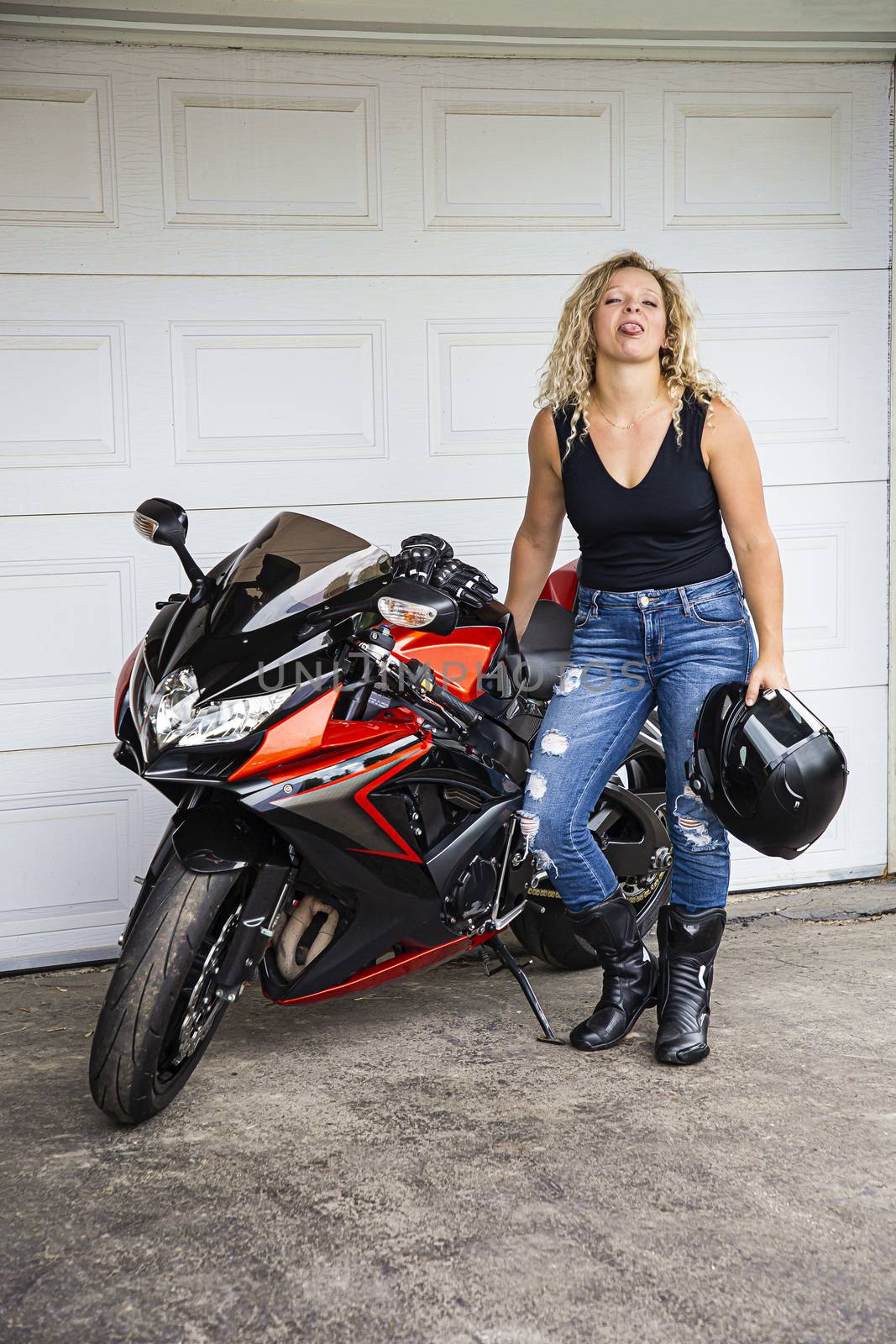 Young motorcycle standing beside her ride, making a face