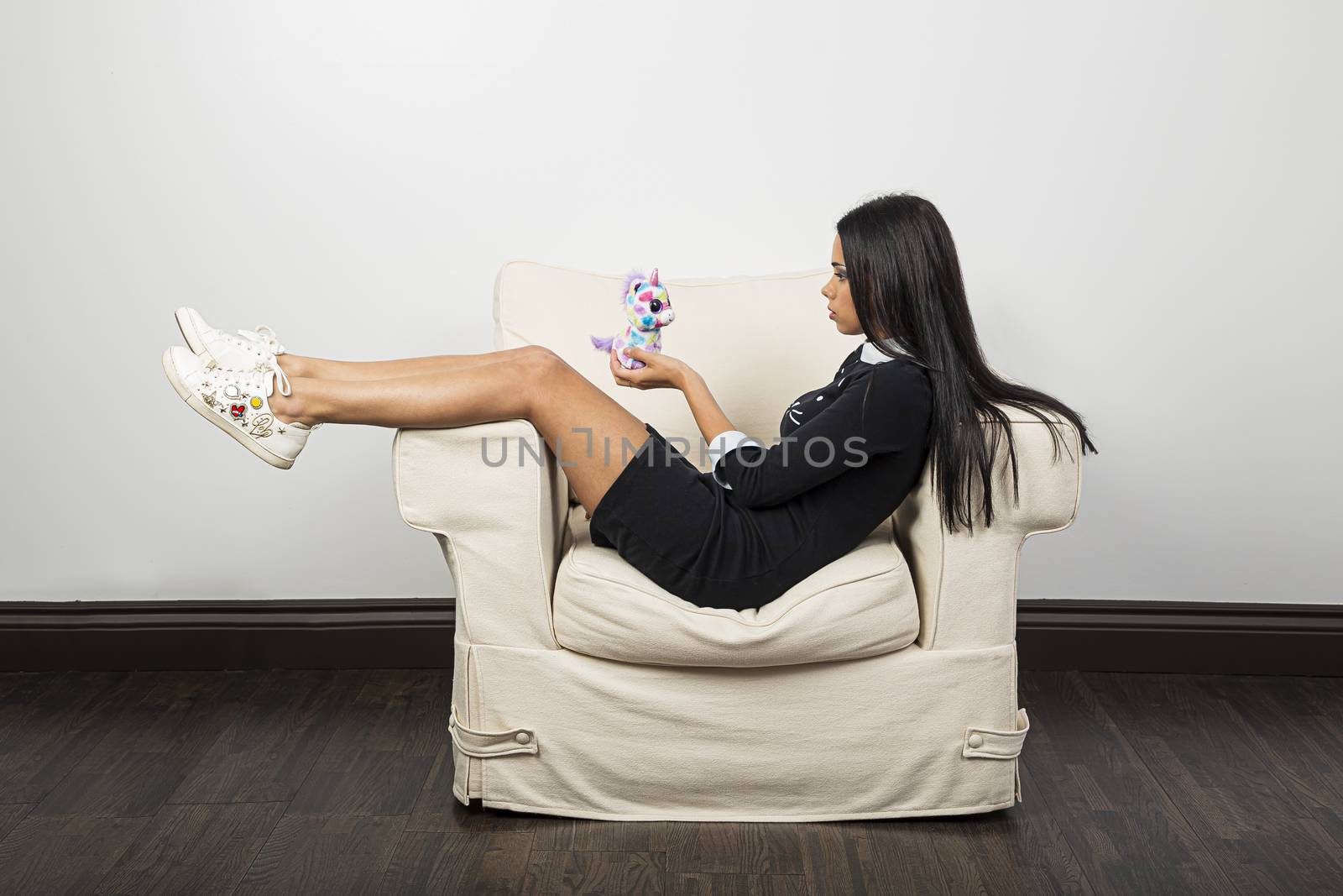 Young woman, with her feet up on a white couch, holding a small plush unicorn