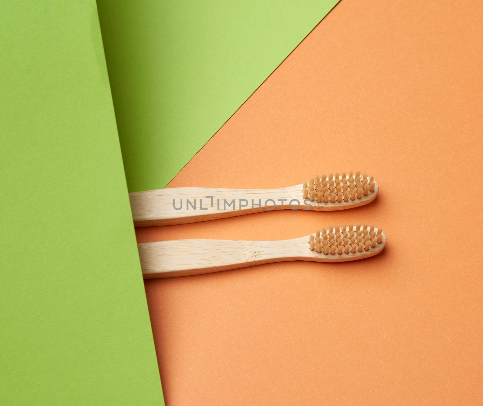 two wooden toothbrushes on a green orange background, plastic rejection concept, zero waste 