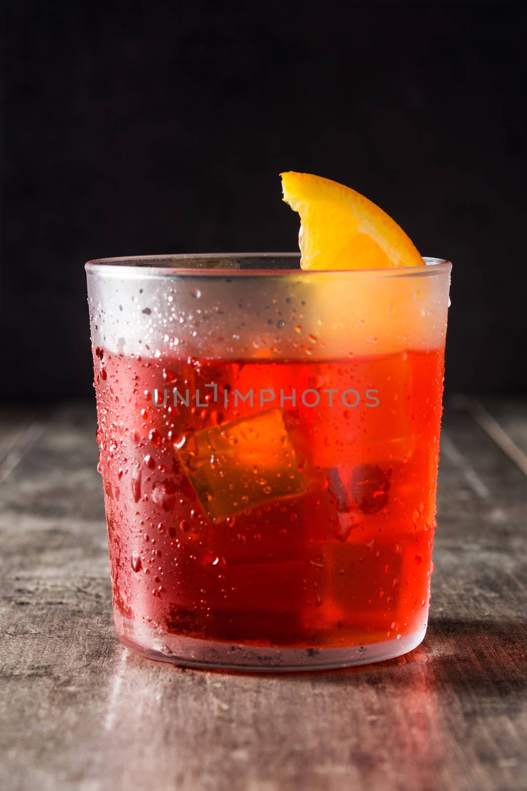 Negroni cocktail with piece of orange in glass on wooden table