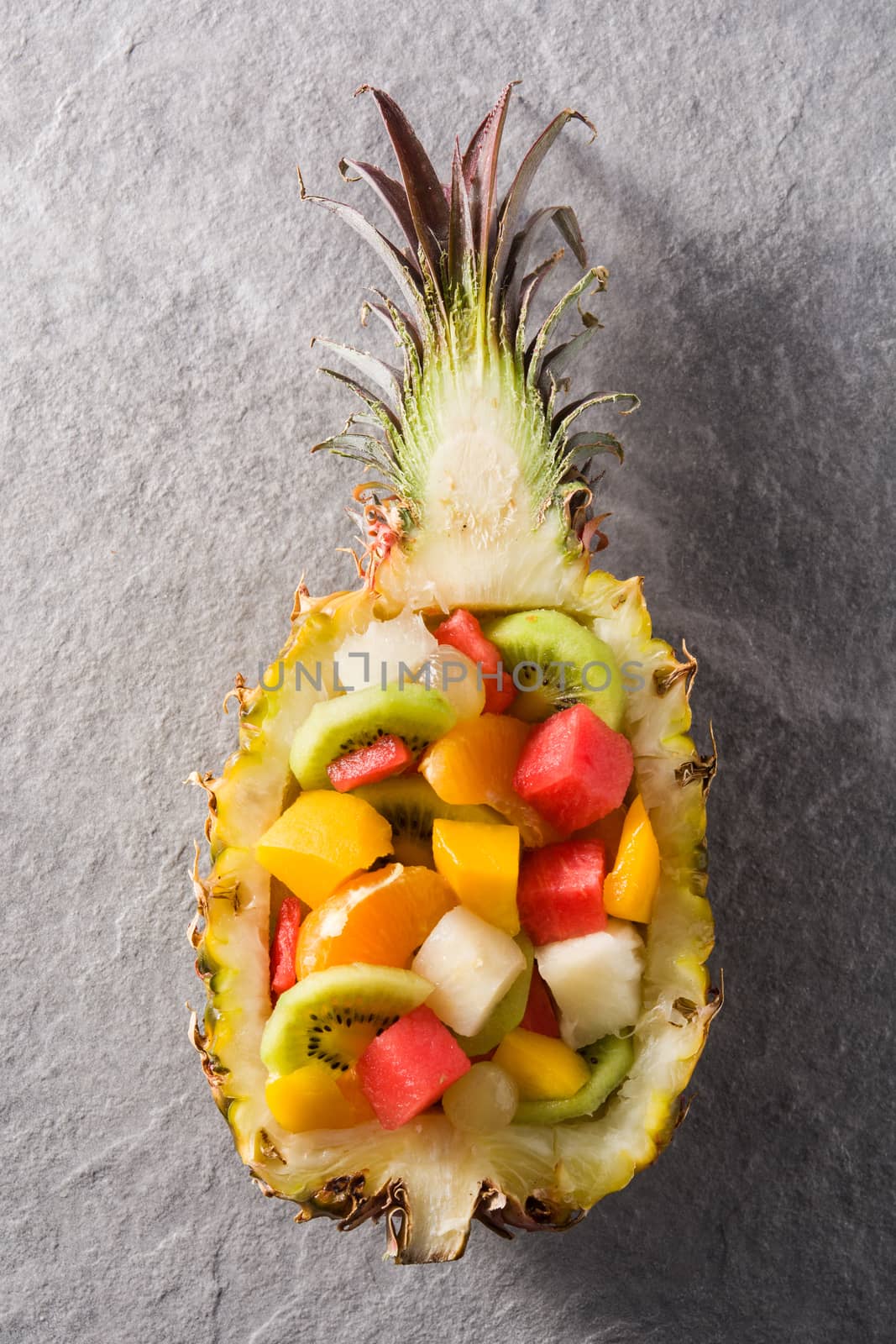 Mix fruit served inside pineapple on gray stone background