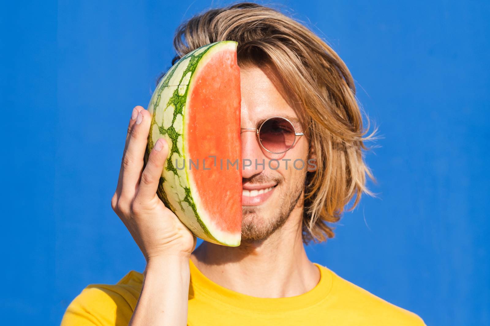 Young man with long blond hair with watermelon by Dumblinfilms