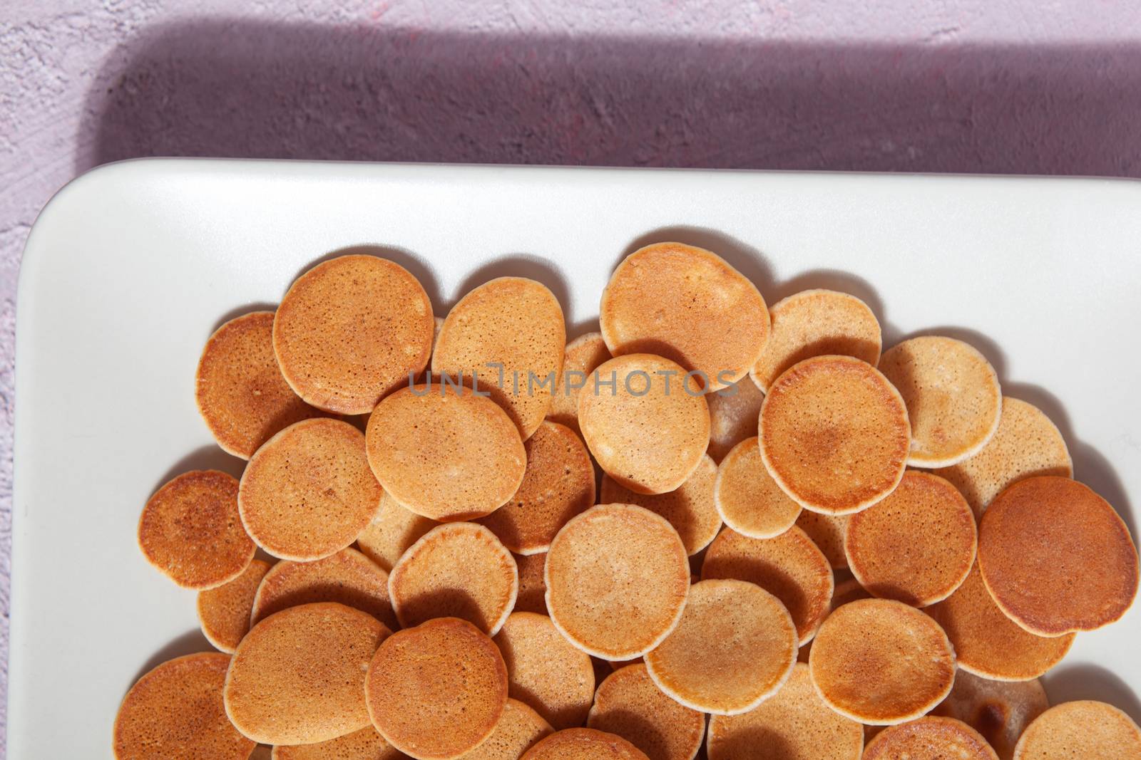 Trendy homemade breakfast, pancake cereal, mini pancakes on light plate on pink concrete background
