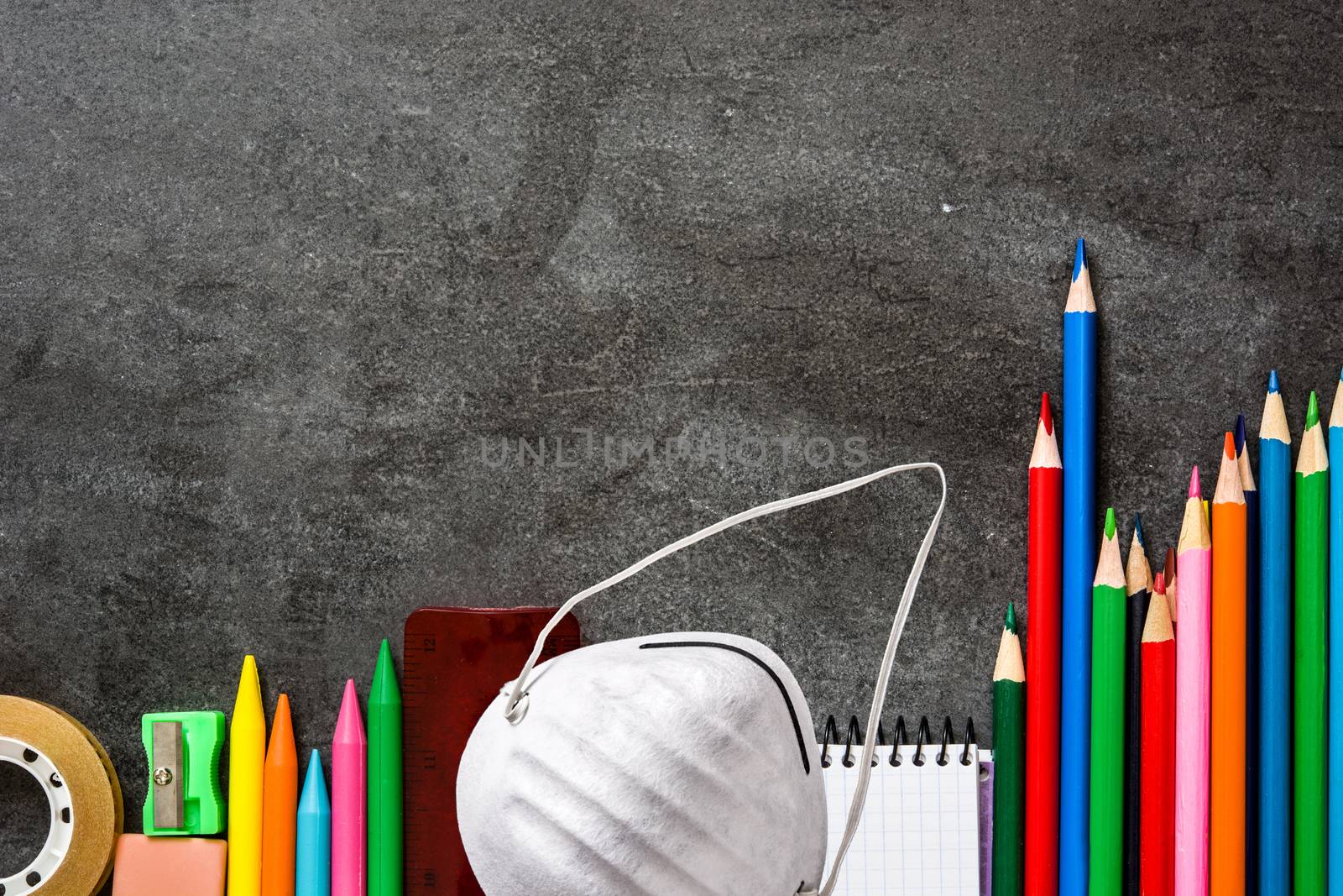 Assortment of school supplies and protective face mask on blackboard background. Back to school concept.