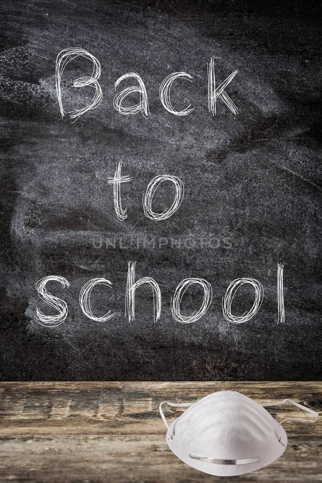 Blackboard with "back to school" message and protective face mask on wooden table.Back to school and coronavirus COVID-19 concept