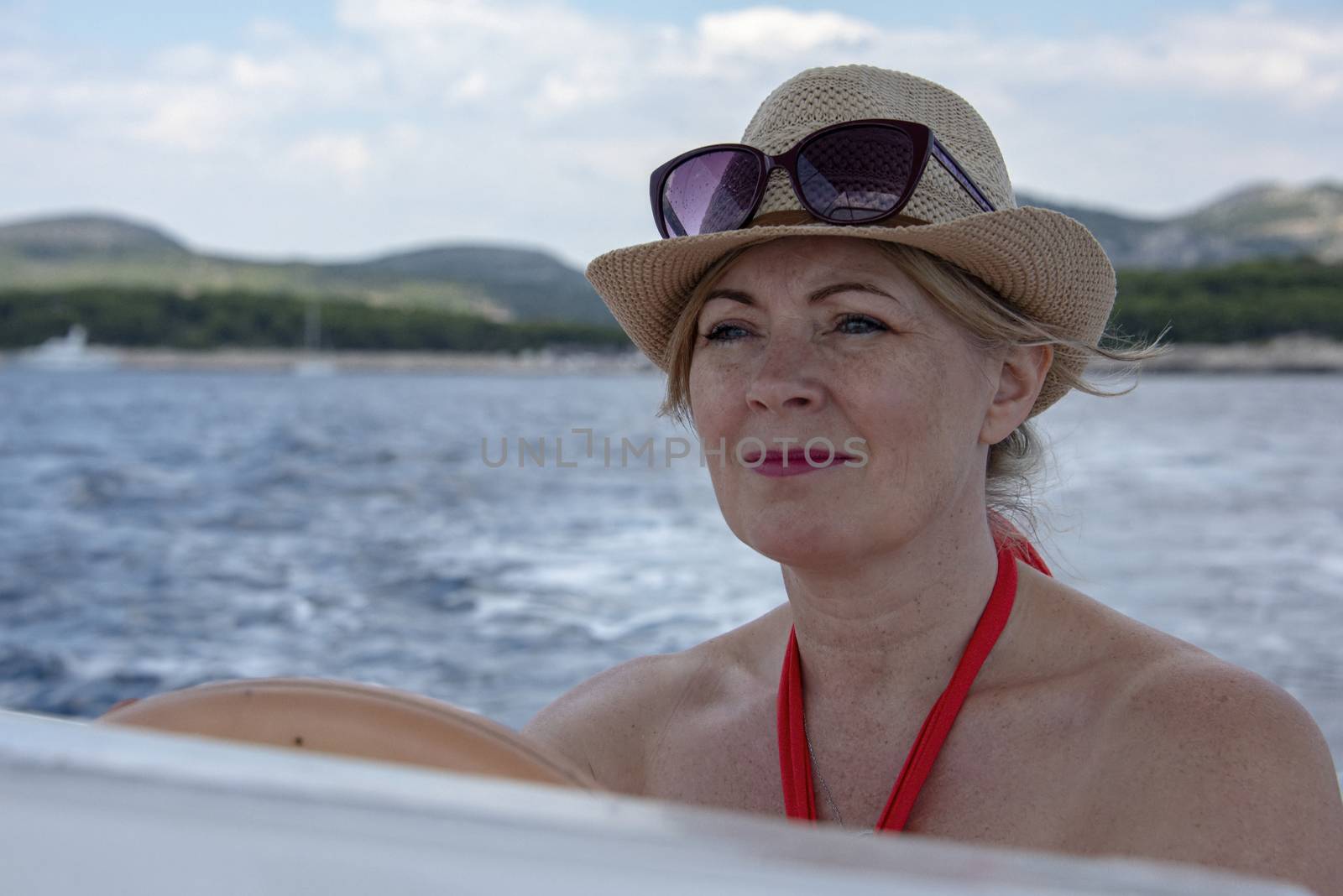 Croatia, Hvar - June 2018: Women in mid 40`s driving a small boat. She wears a straw hat and sunglassed perched on her head.