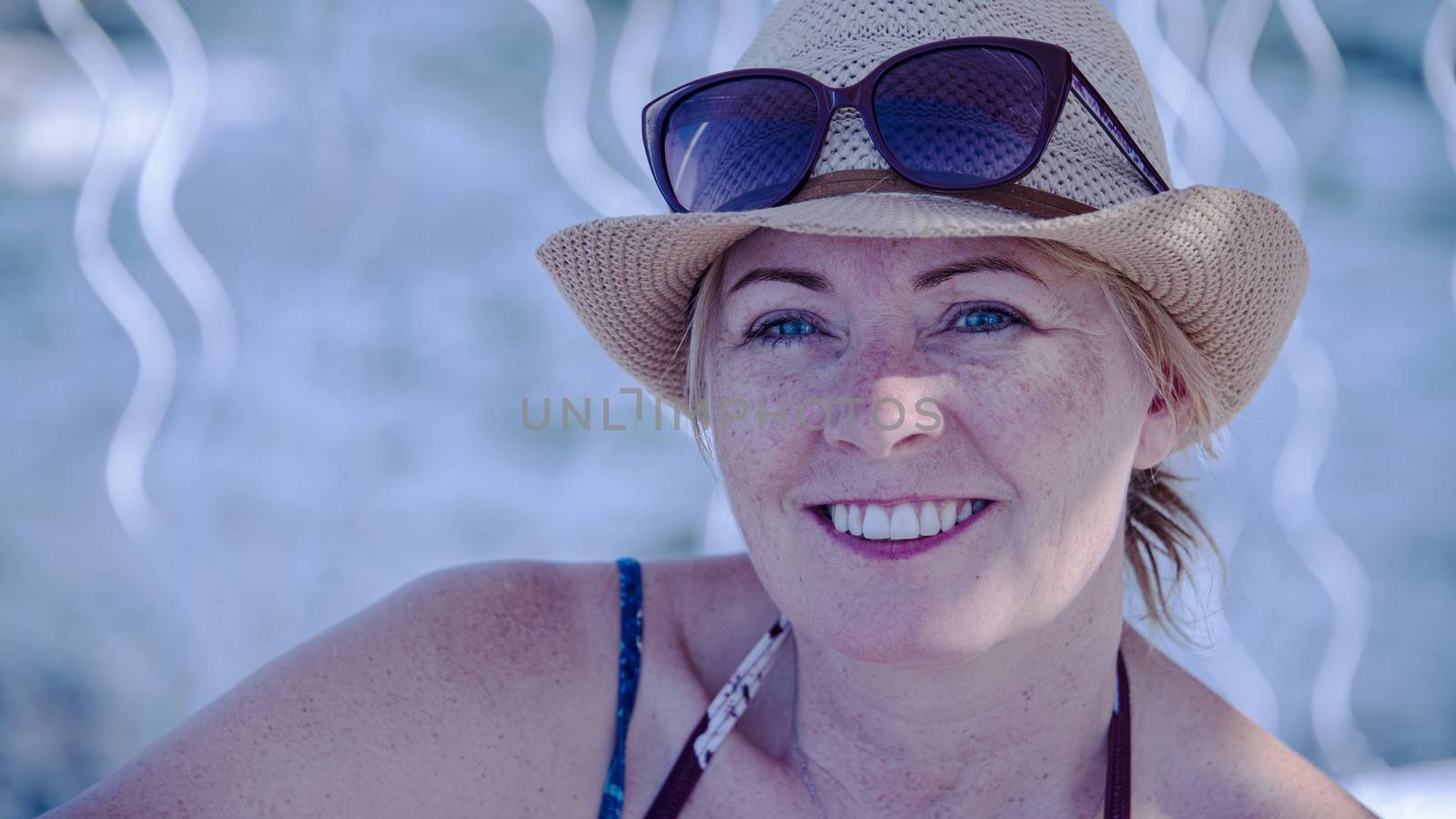 Croatia, Hvar - June 2018: Woman, caucasian, mid 40's, wearing a hat and sunglasses on her head sitting in the shade at beach resort	