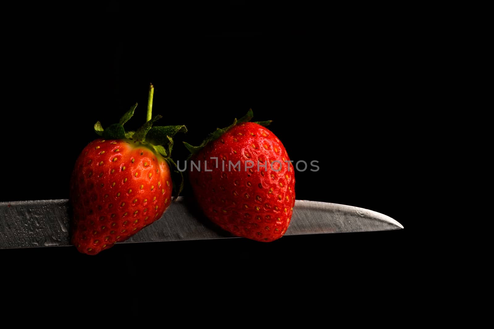 Red Berries balancing on a knife blade with a black background