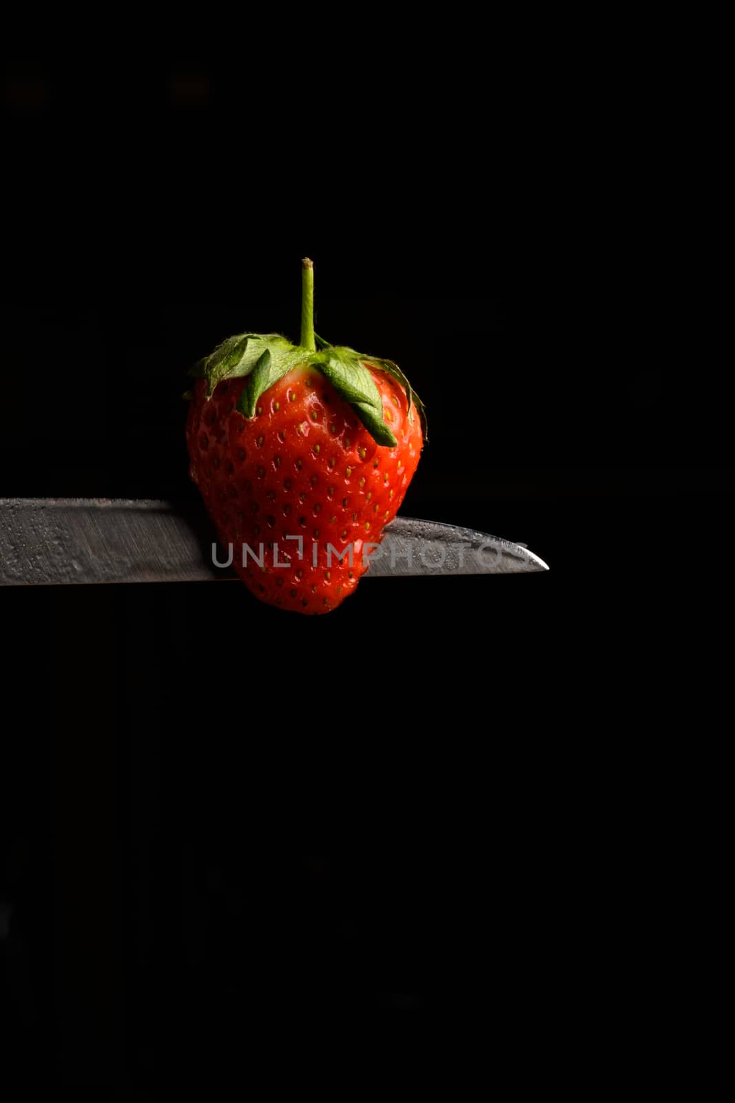 Strawberry balancing on a knife blade with a black background