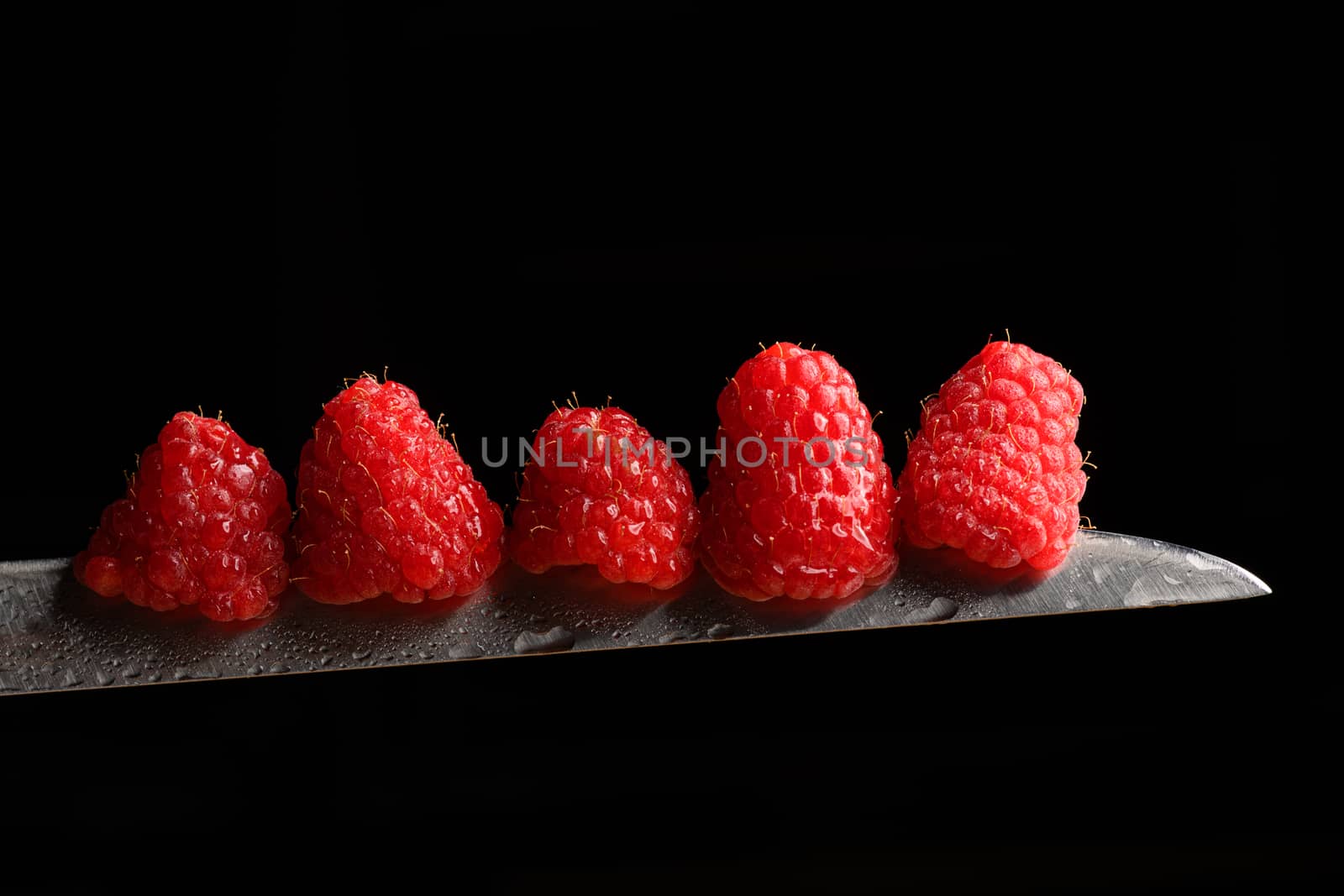 Red Berries balancing on a knife blade with a black background