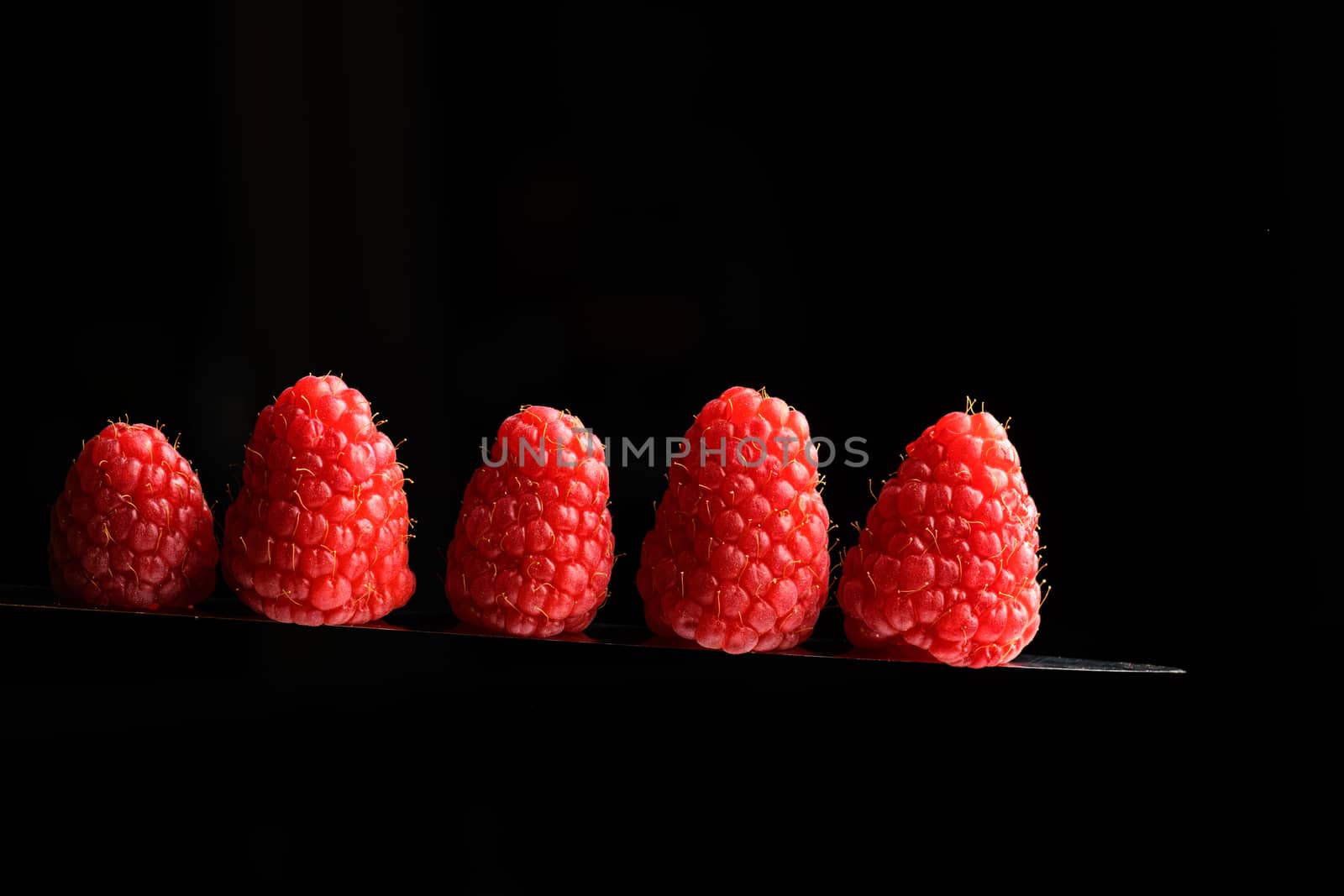 Red Berries balancing on a knife blade with a black background