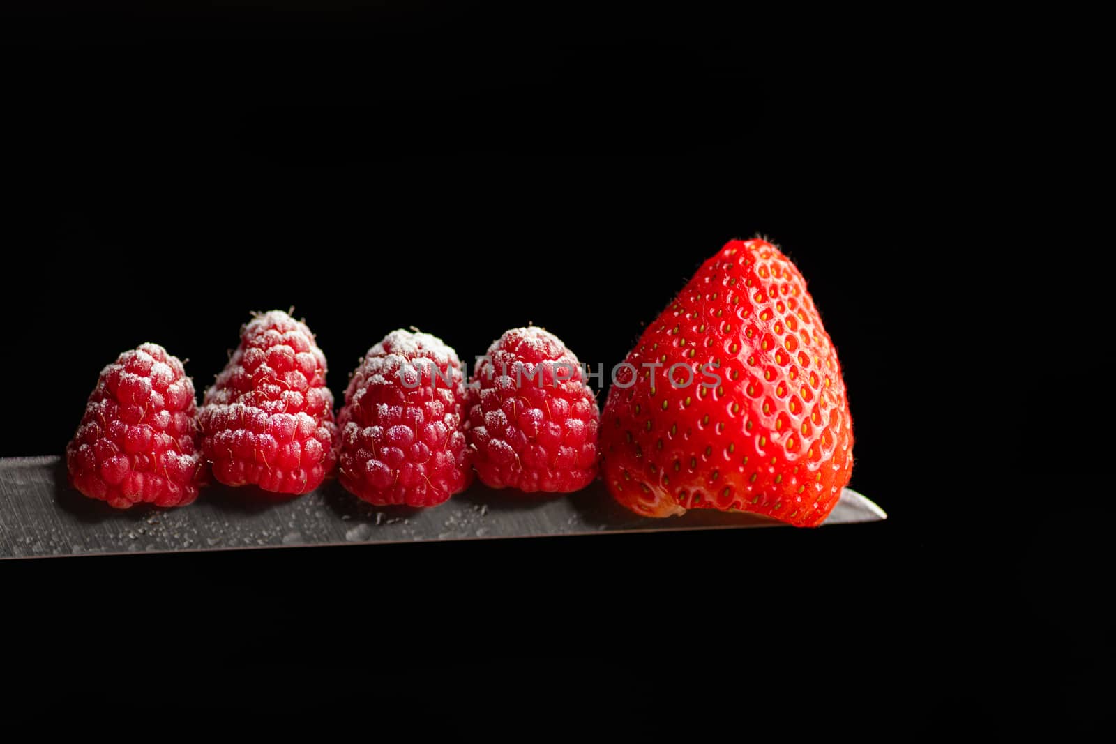 Red Berries balancing on a knife blade with a black background