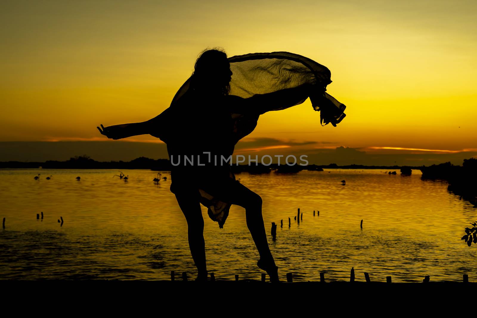 A beautiful latin model is silhouetted as she poses with the rising sun behind her on a exotic Caribbean beach