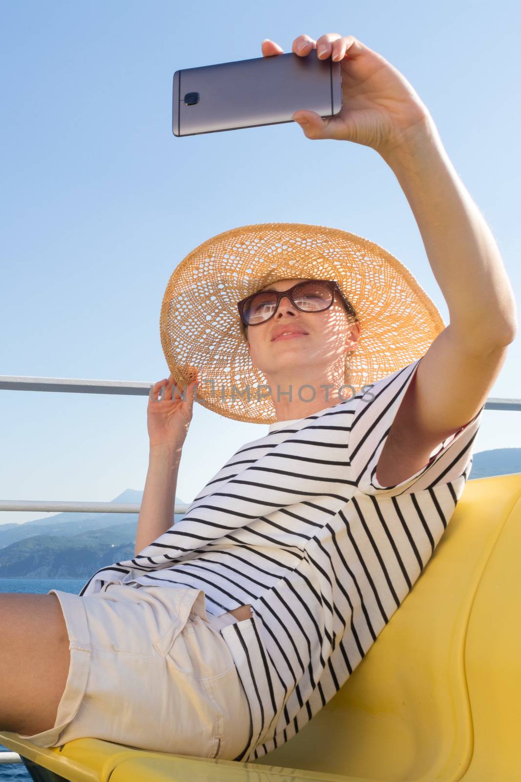 Beautiful, romantic blonde woman taking selfie self portrait photo on summer vacations traveling by cruse ship ferry boat. by kasto