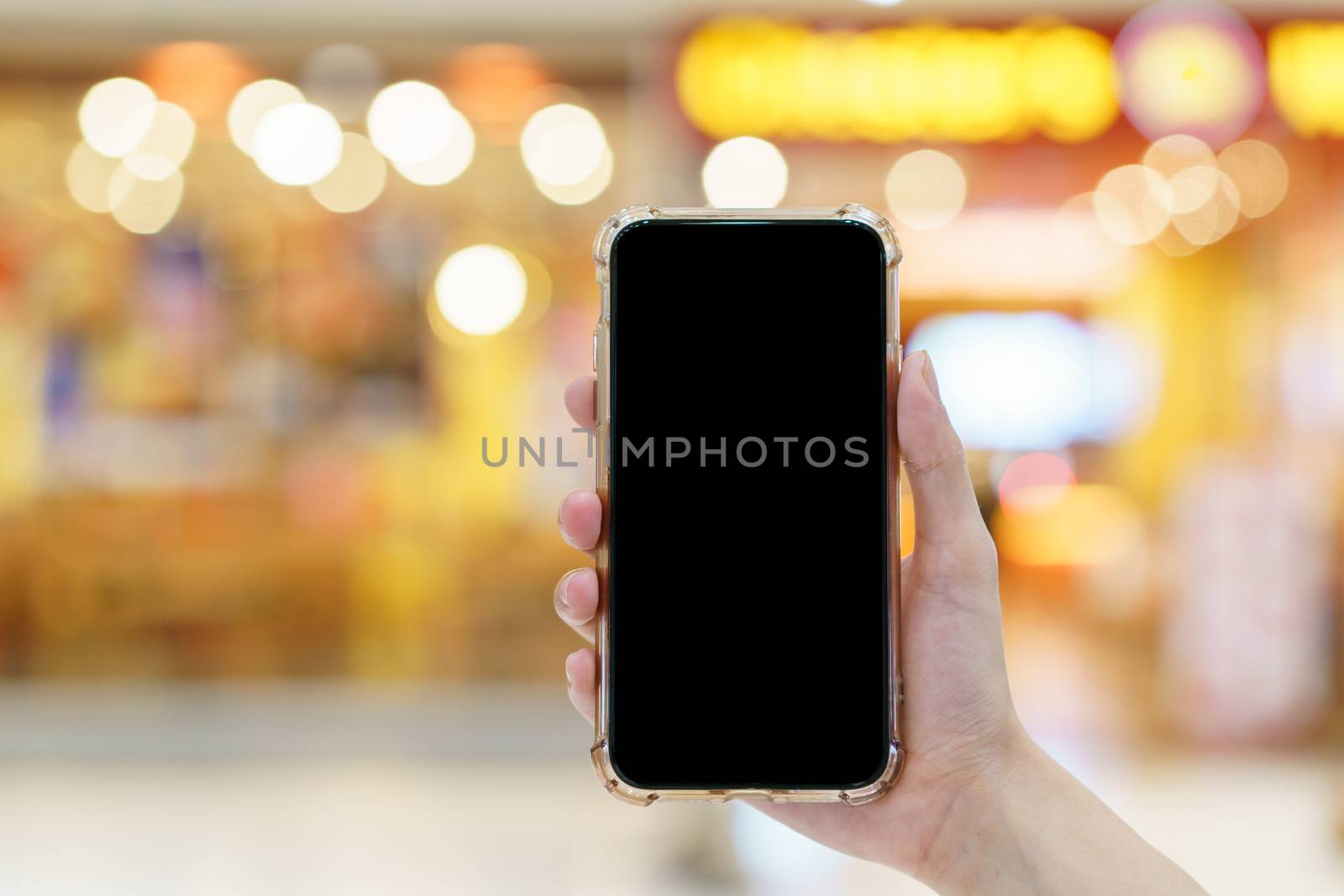Mockup, hands holding blank black screen mobile phone in blurred department store, digital payment concept