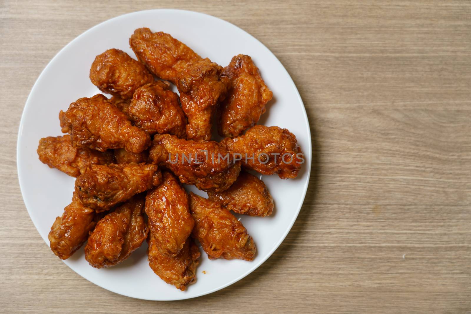 Plate of spicy deep fried chicken wings, Korean food style on wooden table.