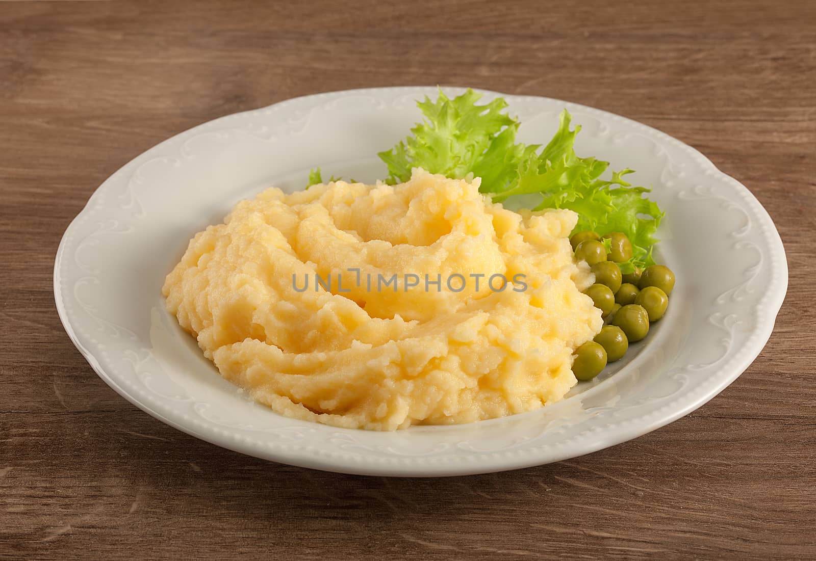 White plate with mashed potatoes, green peas and fresh green lettuce on the wooden table
