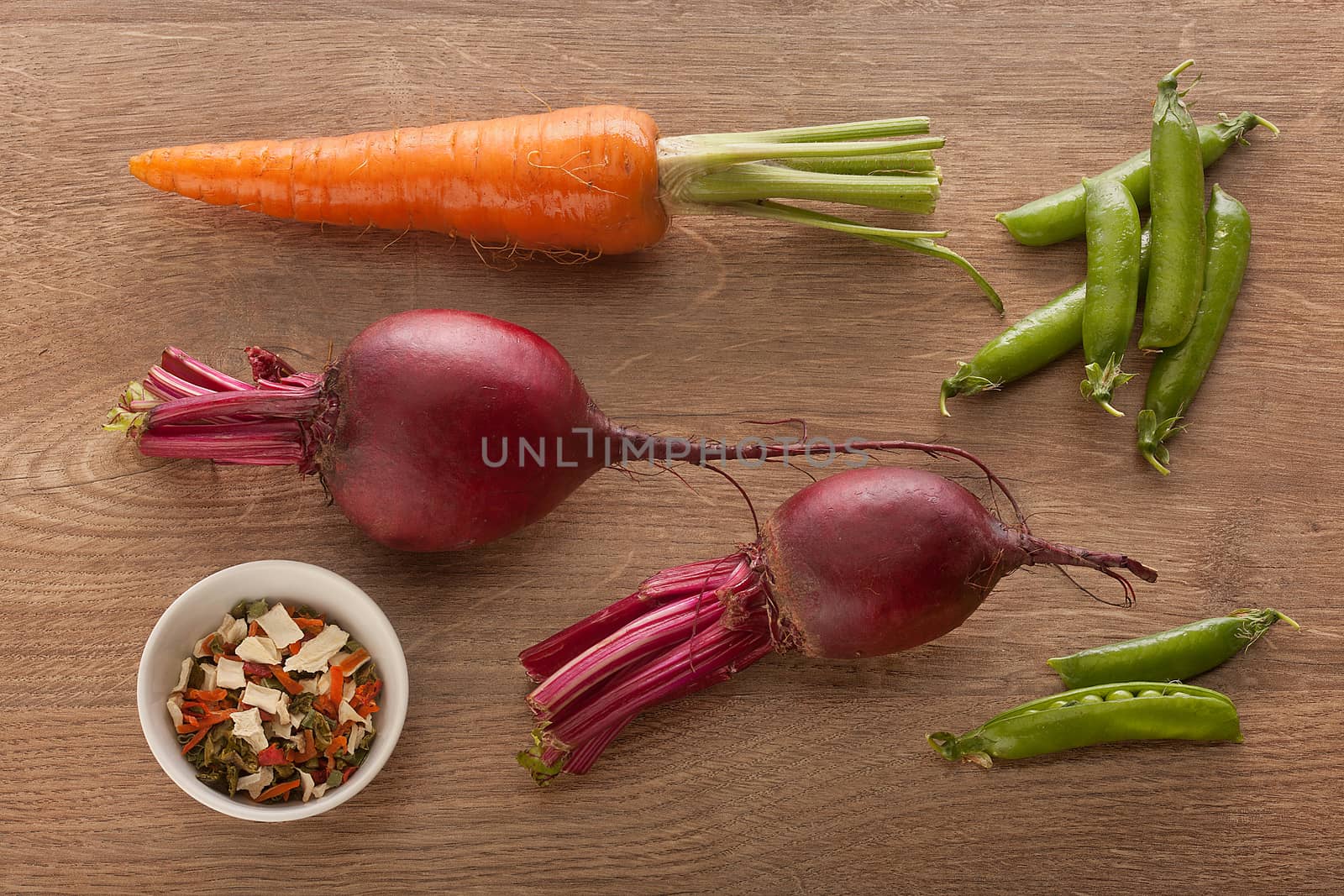 Top view of carrot, two beets, some pea pods and bowl with dried herbs on the wooden table