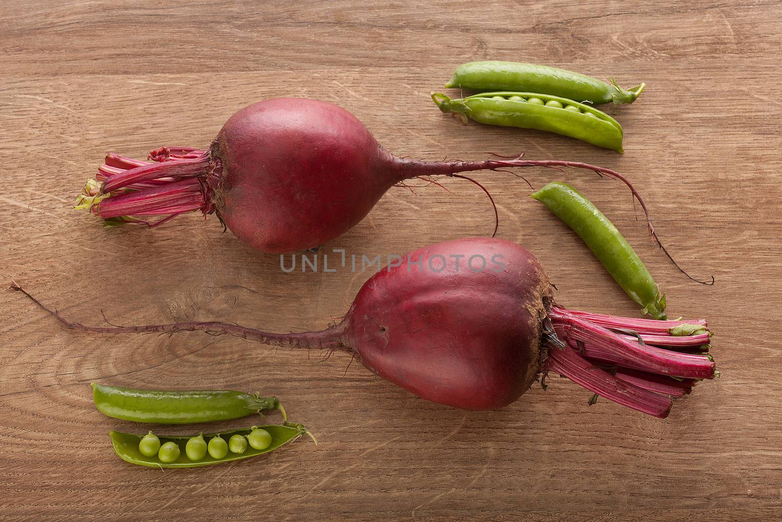 Top view of two red beets and fresh green pea pods on the wooden table