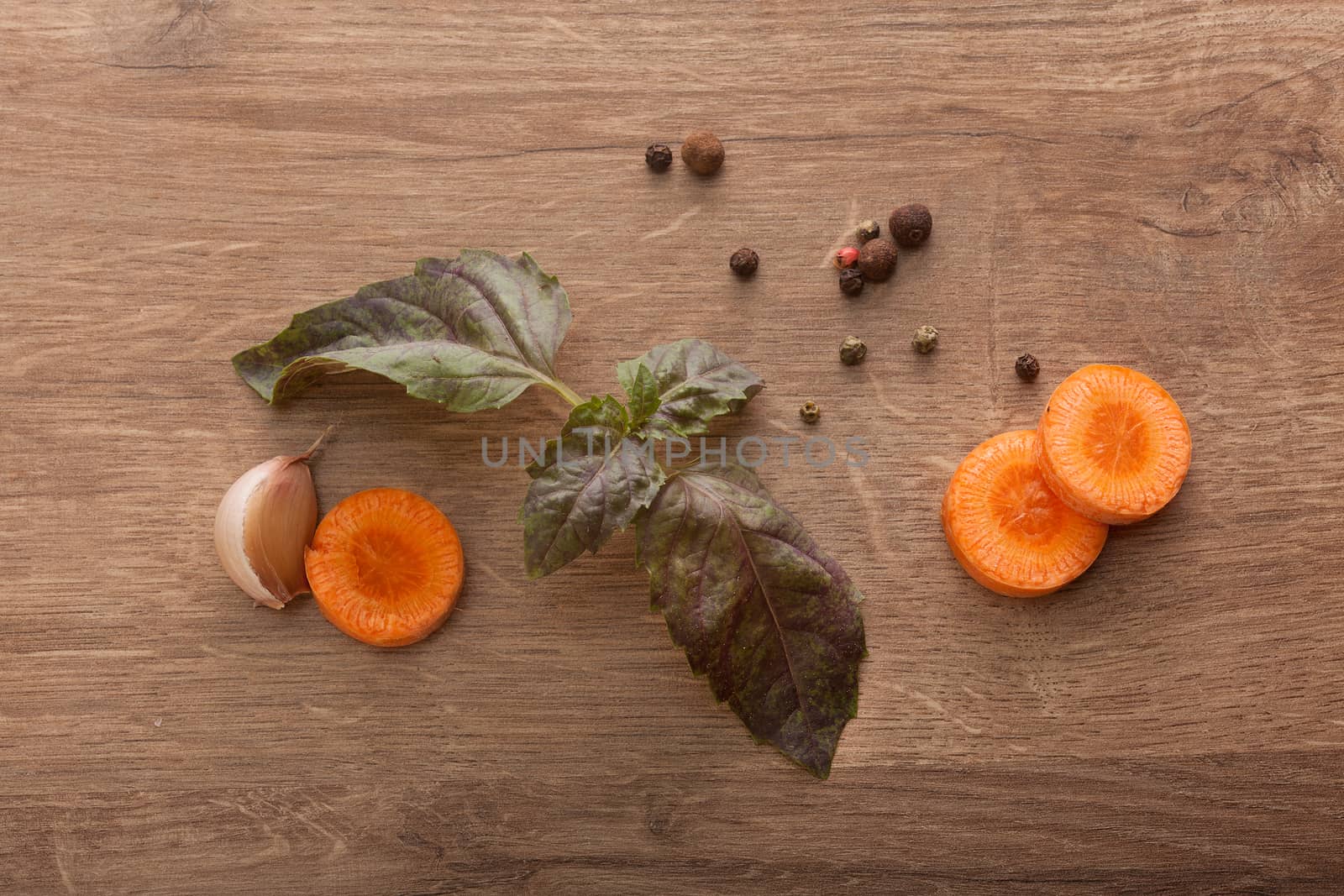 Top view of carrot's slices, clove of garlic, branch of fresh basil and black peppers on the wooden table