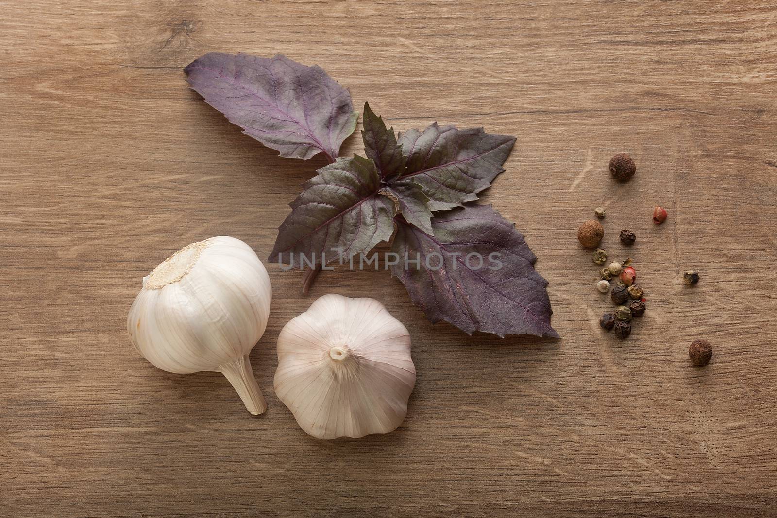 Top view of purple basil, two head of garlic and black peppers on the wooden table