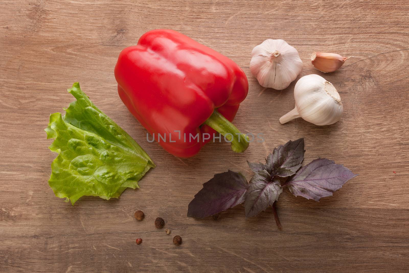 Top view of whole red paprika, purple basil, head and cloves of garlic, green lettuce and black pepper on the wooden table