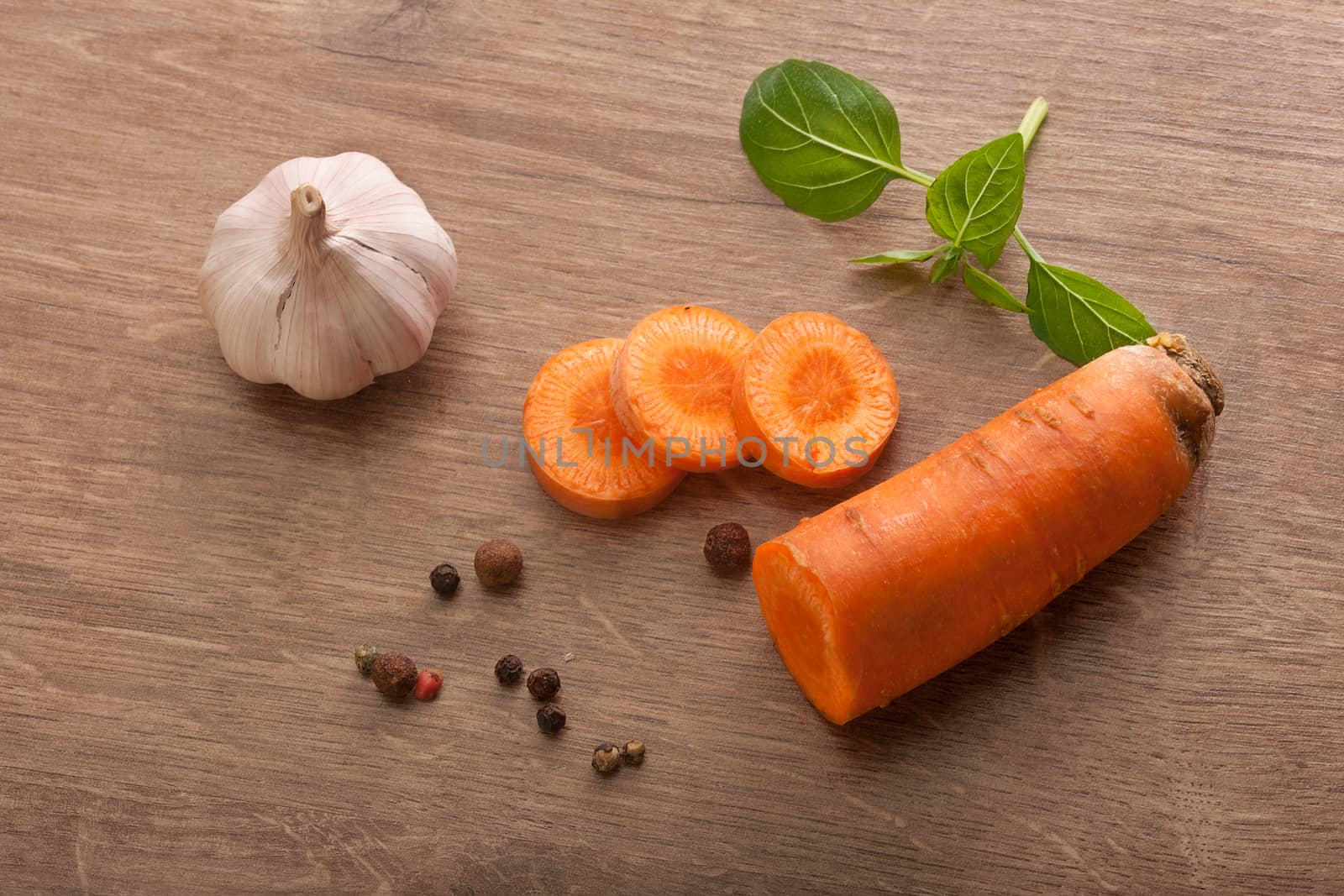 Top view of carrot, fresh green basil; head of garlic and black peppers on the wooden table