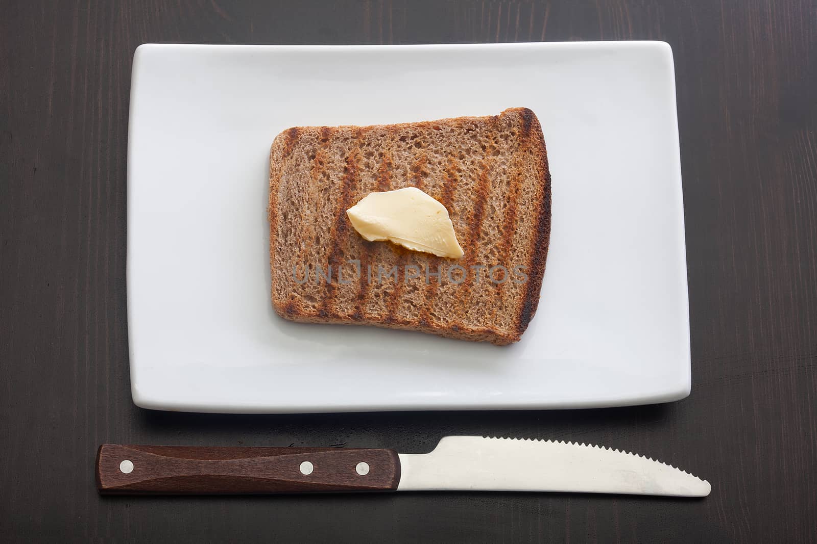 Top view of toasted rye bread with butter on the white plate