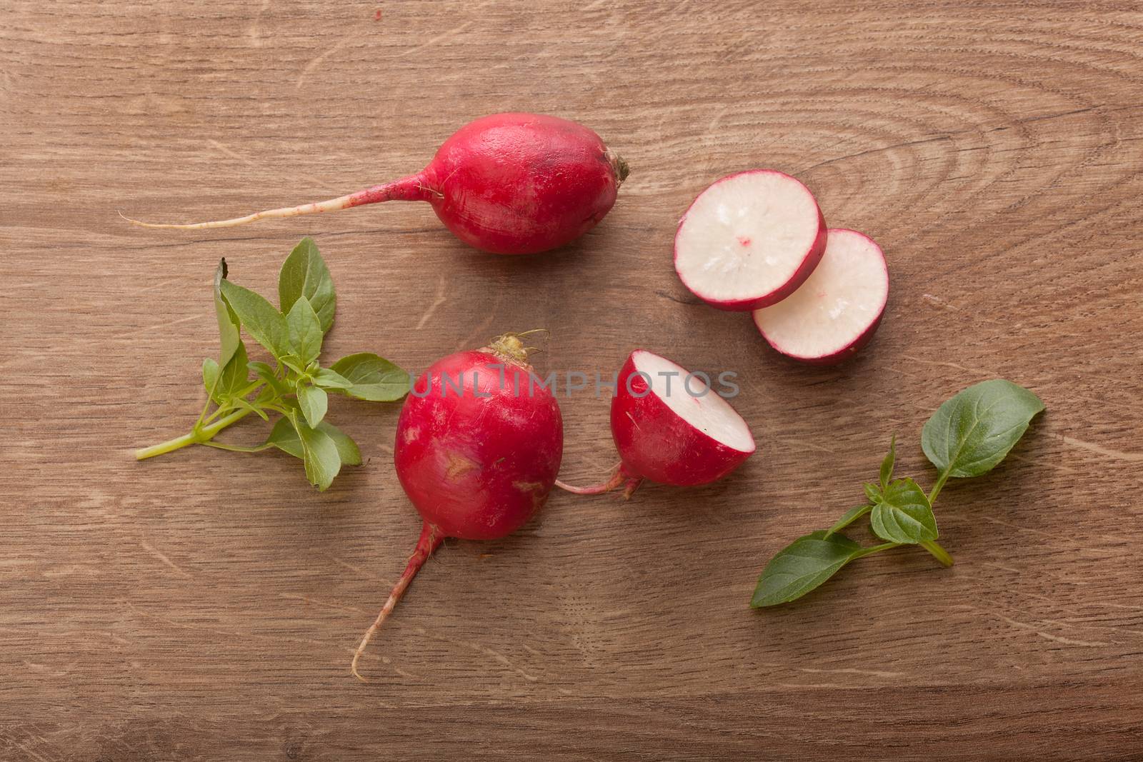 Top view of whole and sliced red radish with fresh green basil on the wooden table