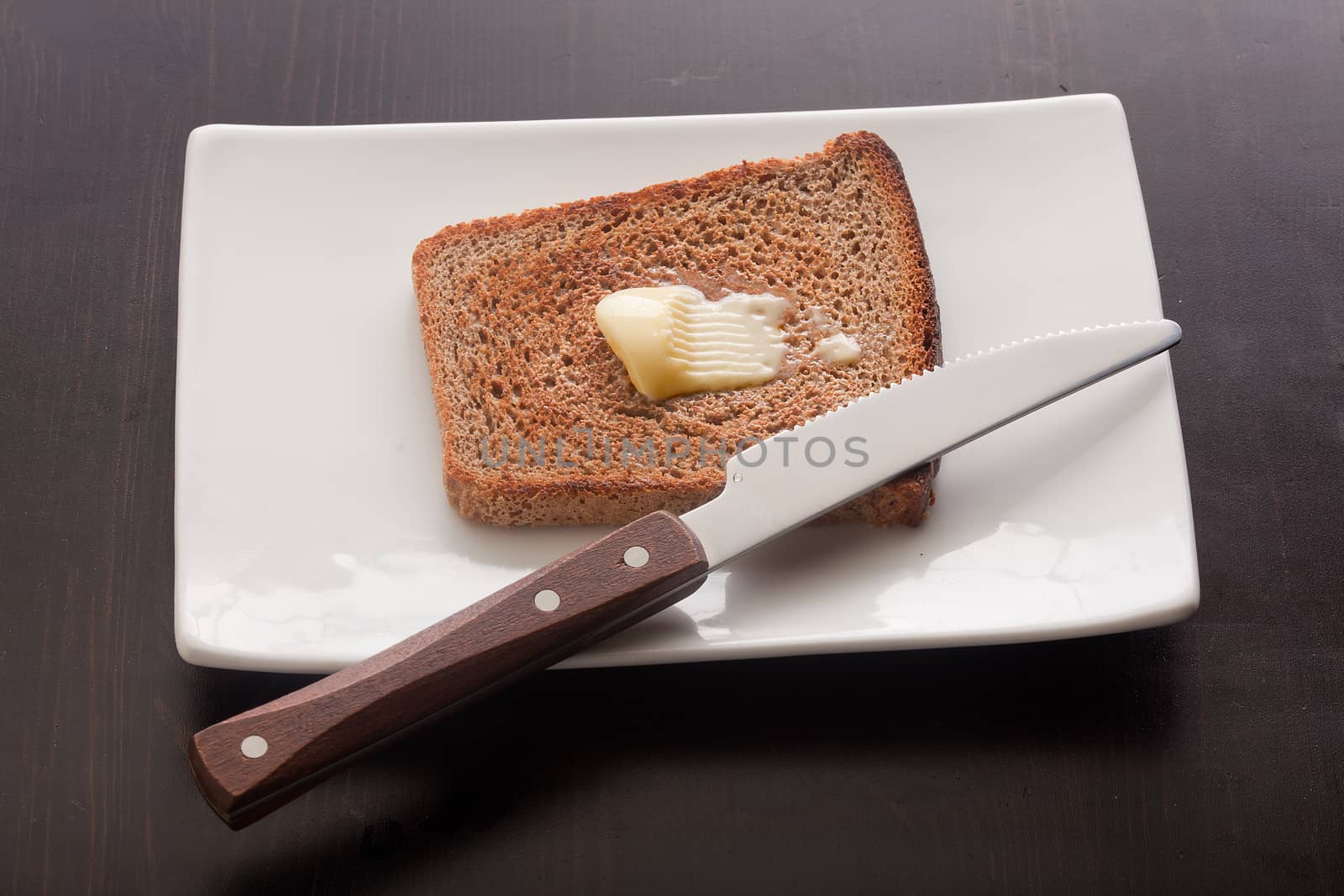 Top view of toasted rye bread with butter on the white plate