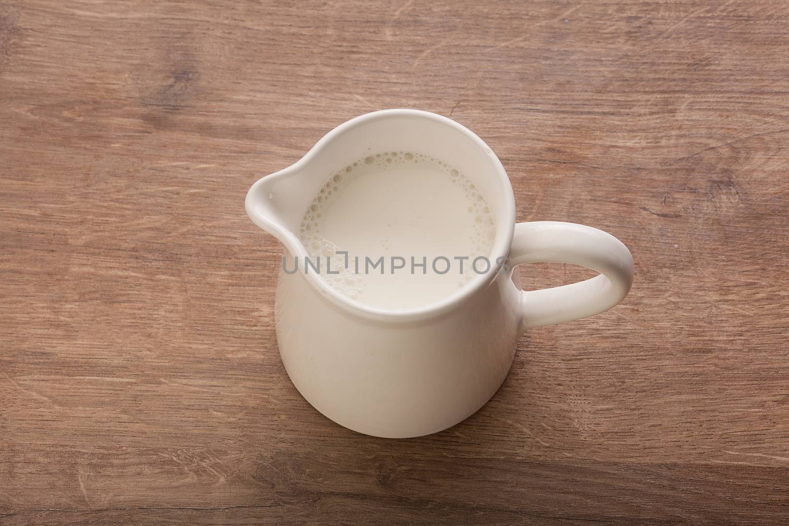 Top view of white pitcher with milk on the wooden table