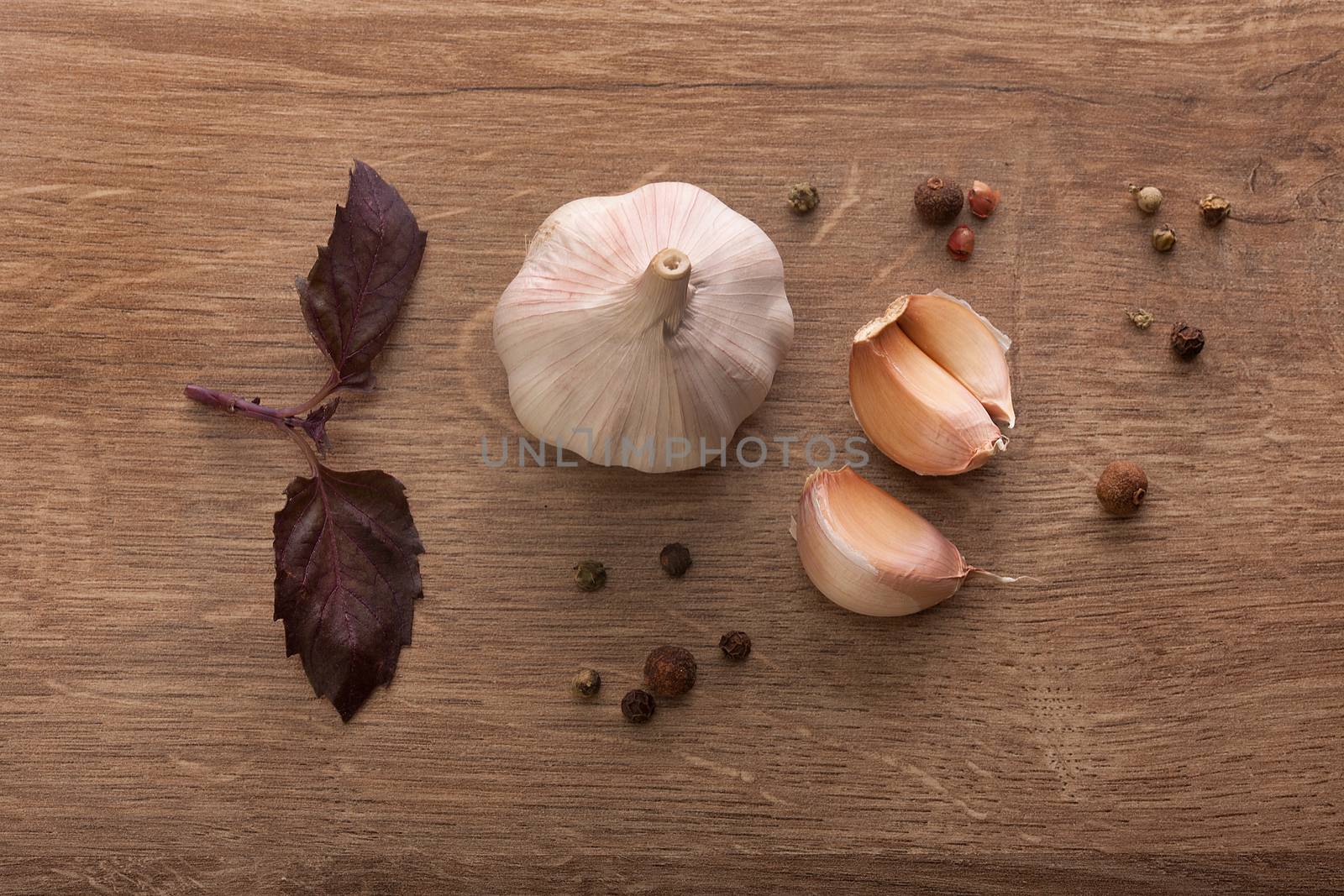 Top view of head and cloves of garlic, purple basil and black pepper on the wooden table