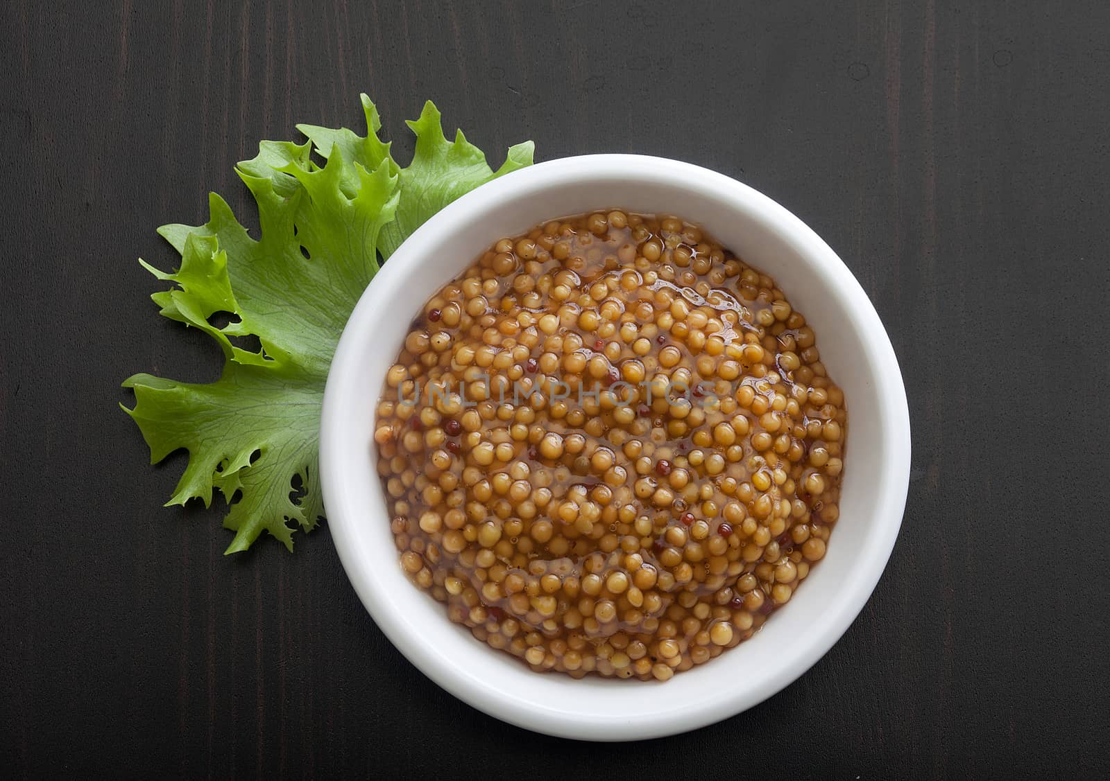 Top view of white plate with grainy mustard and fresh green lettuce on the black wooden table