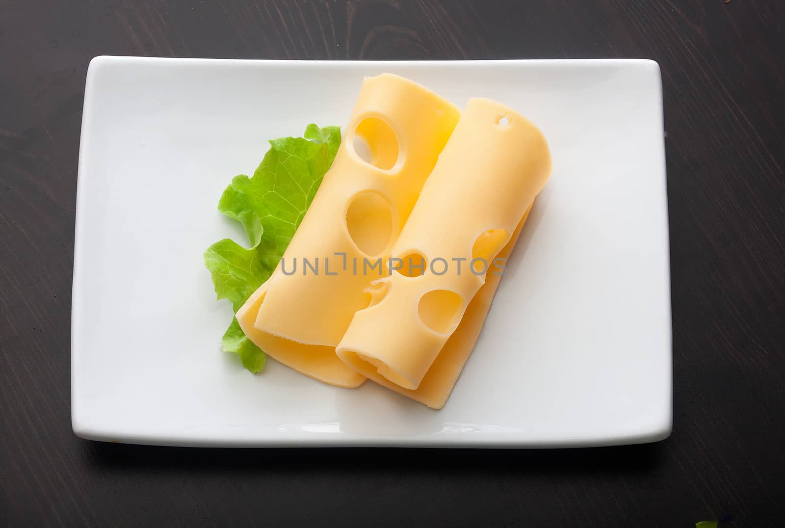 Top view of white plate with two pieces of maasdam cheese and leaf of grenn fresh lettuce