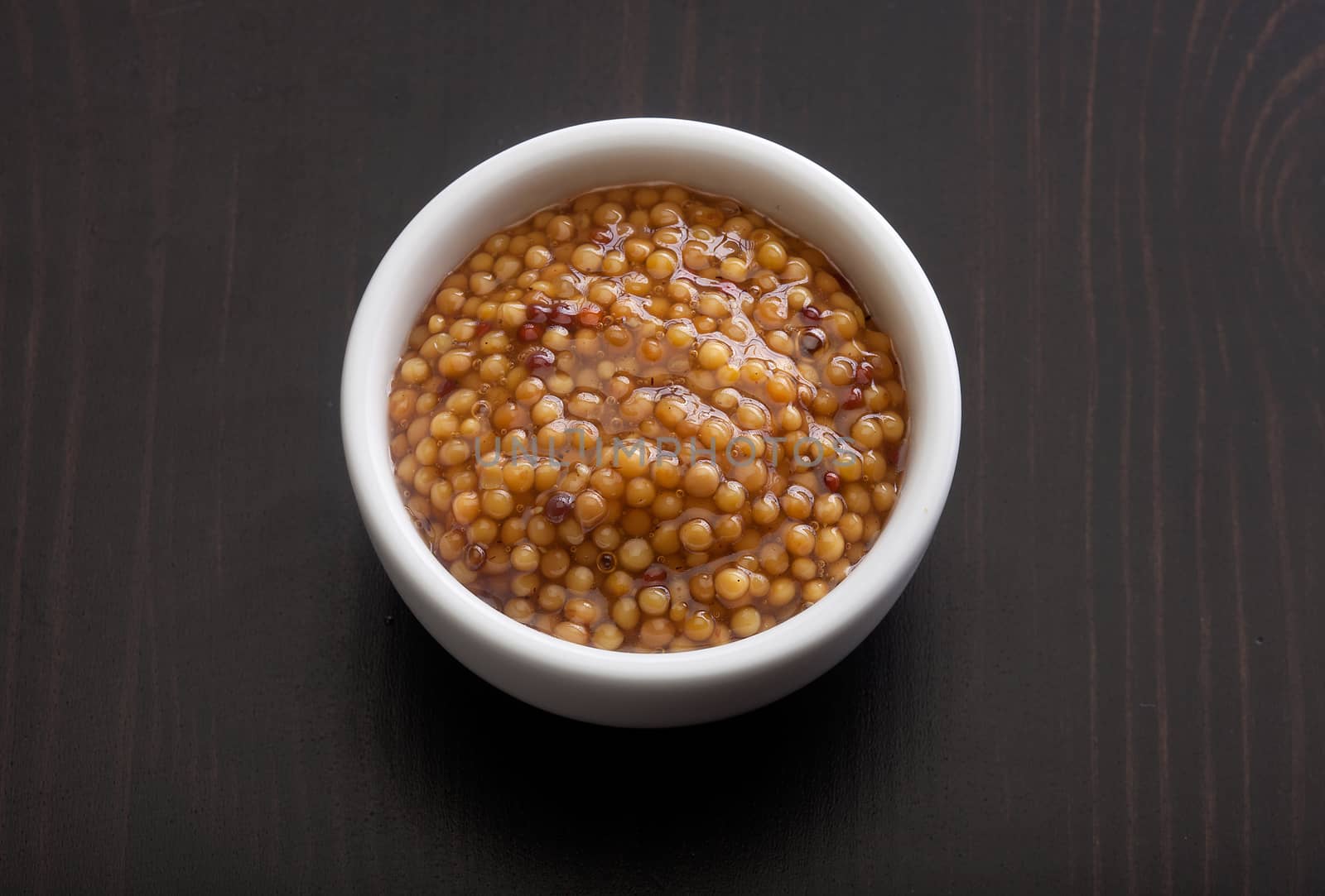 Top view of white plate with grainy mustard on the black wooden table