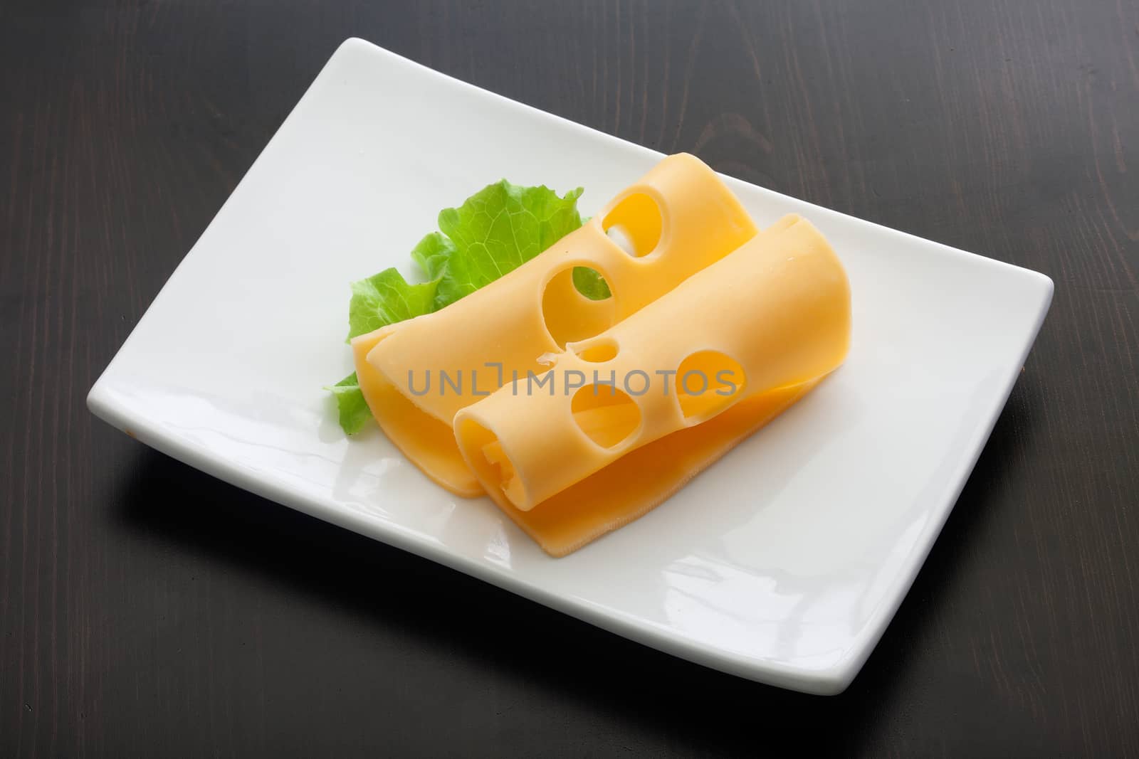 White plate with two pieces of maasdam cheese and fresh green lettuce on the black wooden table