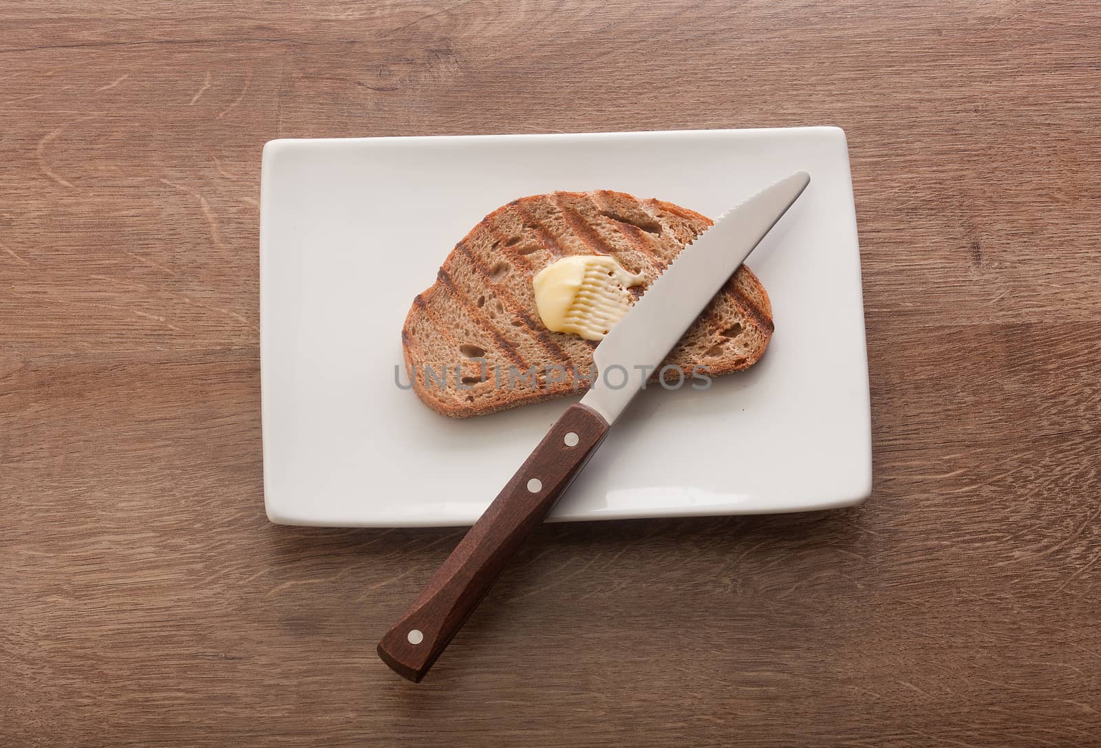 Top view of toasted rye bread with butter on the white plate