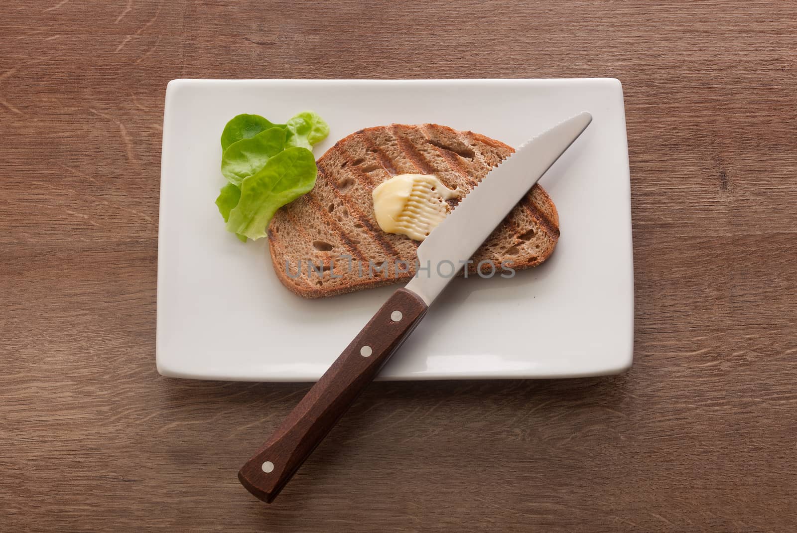 Top view of toasted rye bread with butter and lettuce on the white plate