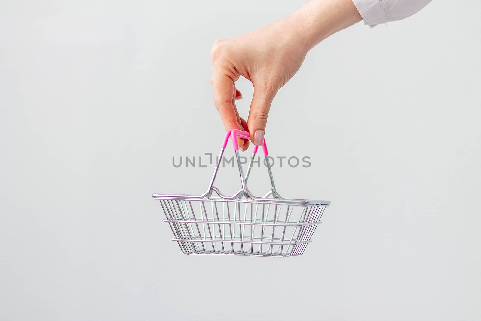 Close-up of a woman's hand horizontally holding a toy small metal shopping basket with a pink plastic handle isolated on a white background. copy space for advertising. The concept of shopping. by Pirlik