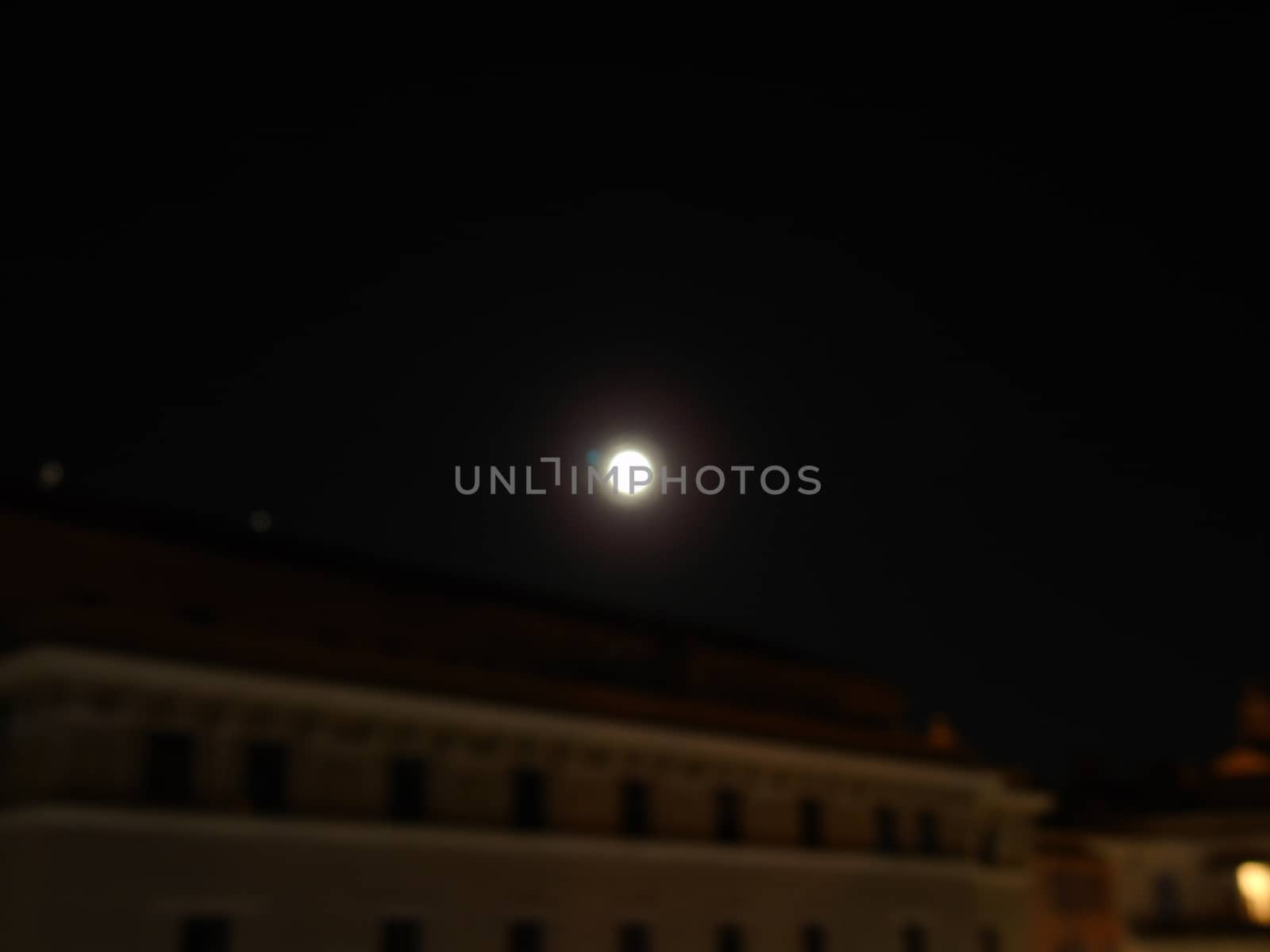 Genova, Italy - 07/05/2020: An amazing photography of the full moon over the city of Genova by night with a great clear and blue sky in the background and some stars.